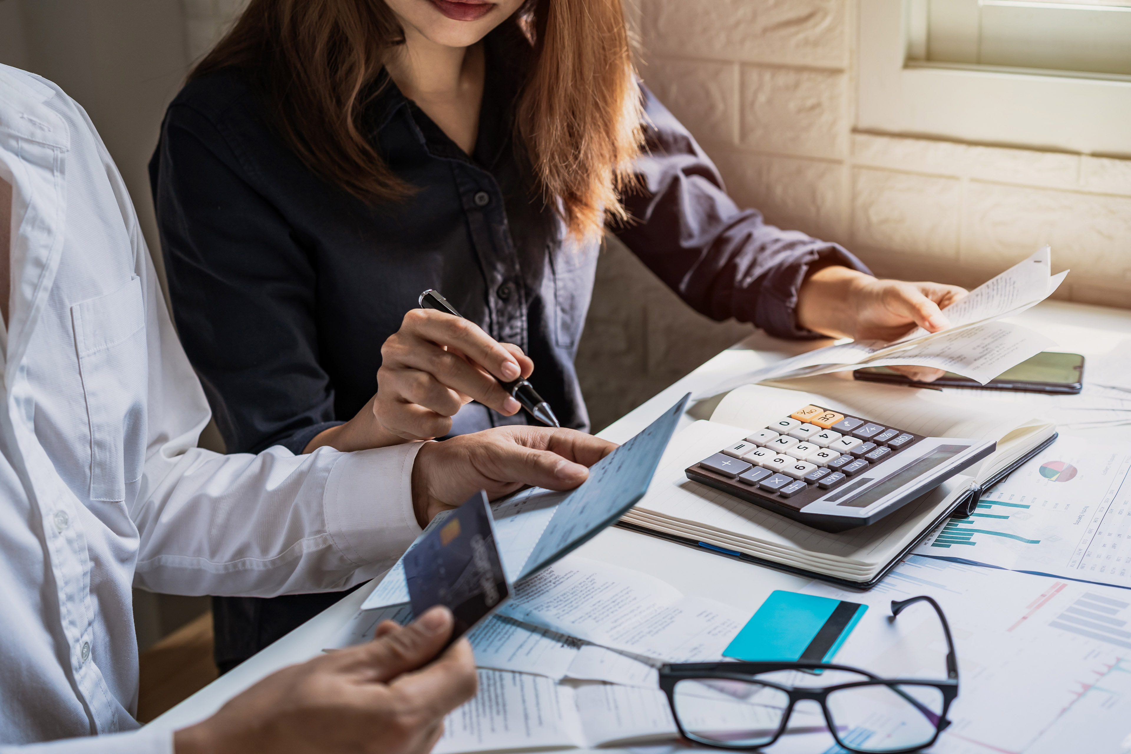 Two people checking bills and using a calculator together at a table at home