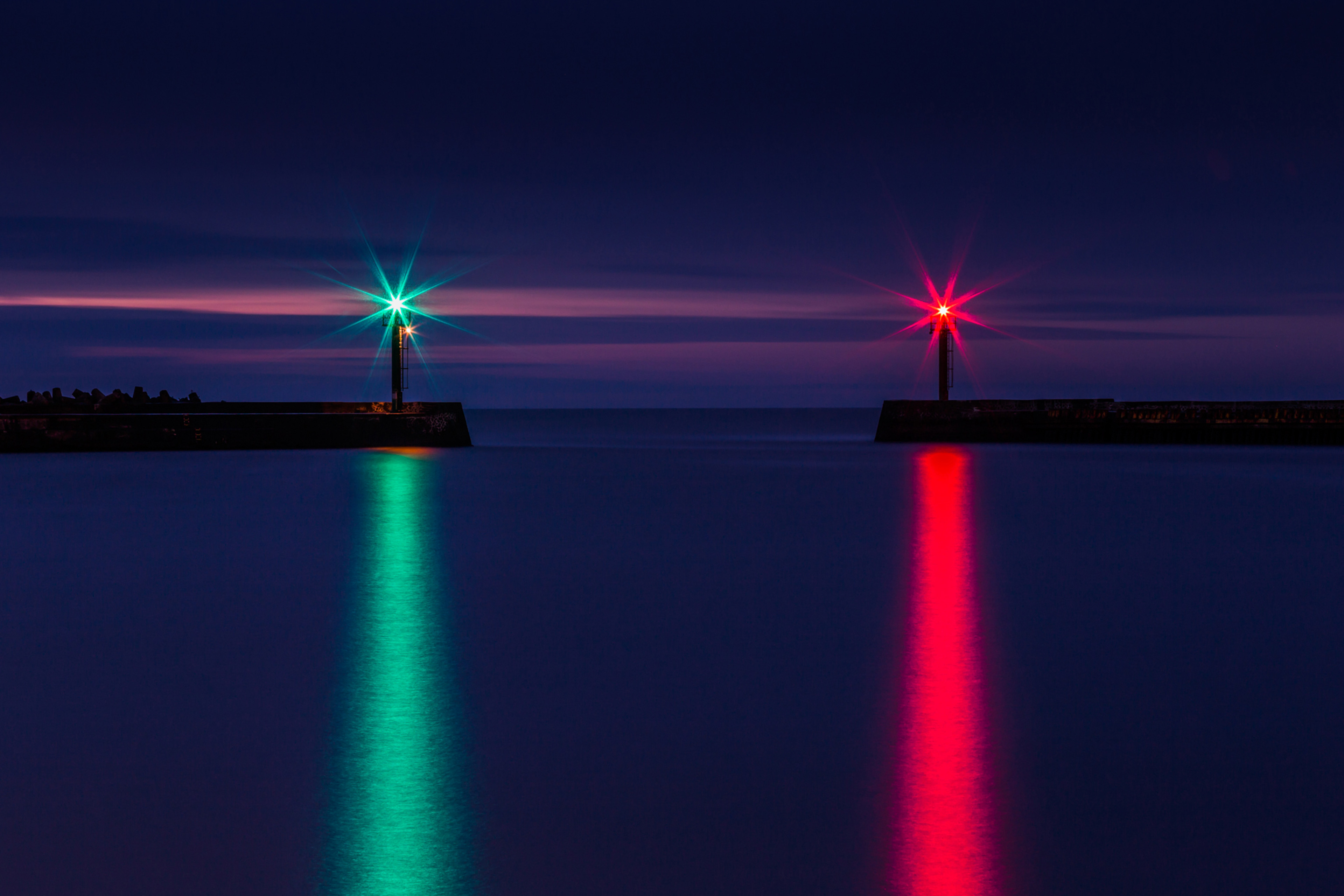 Lights marking a harbour entrance reflected on the sea at dusk