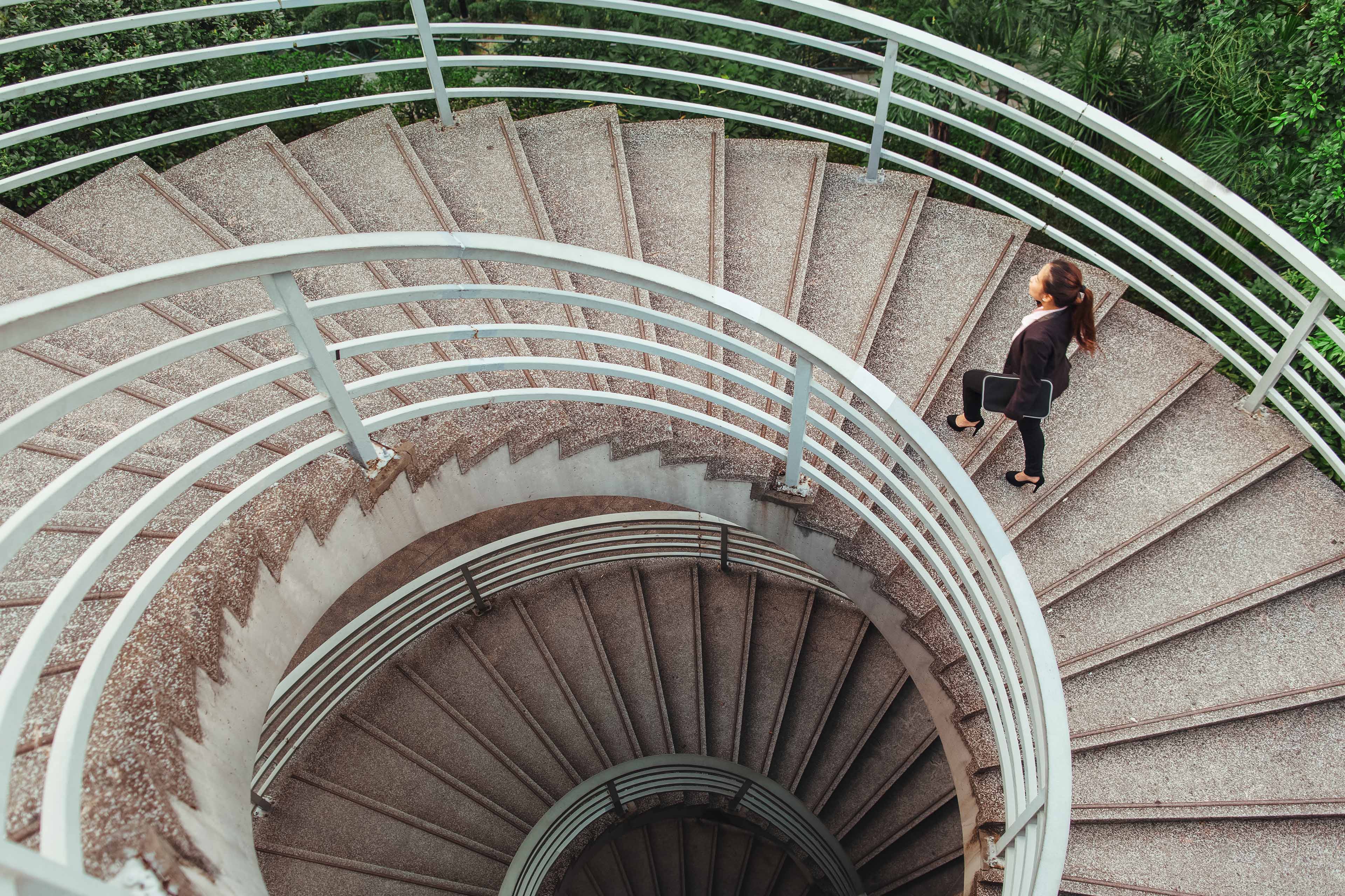 Woman walks down a spiral outdoor staircase, seen from above