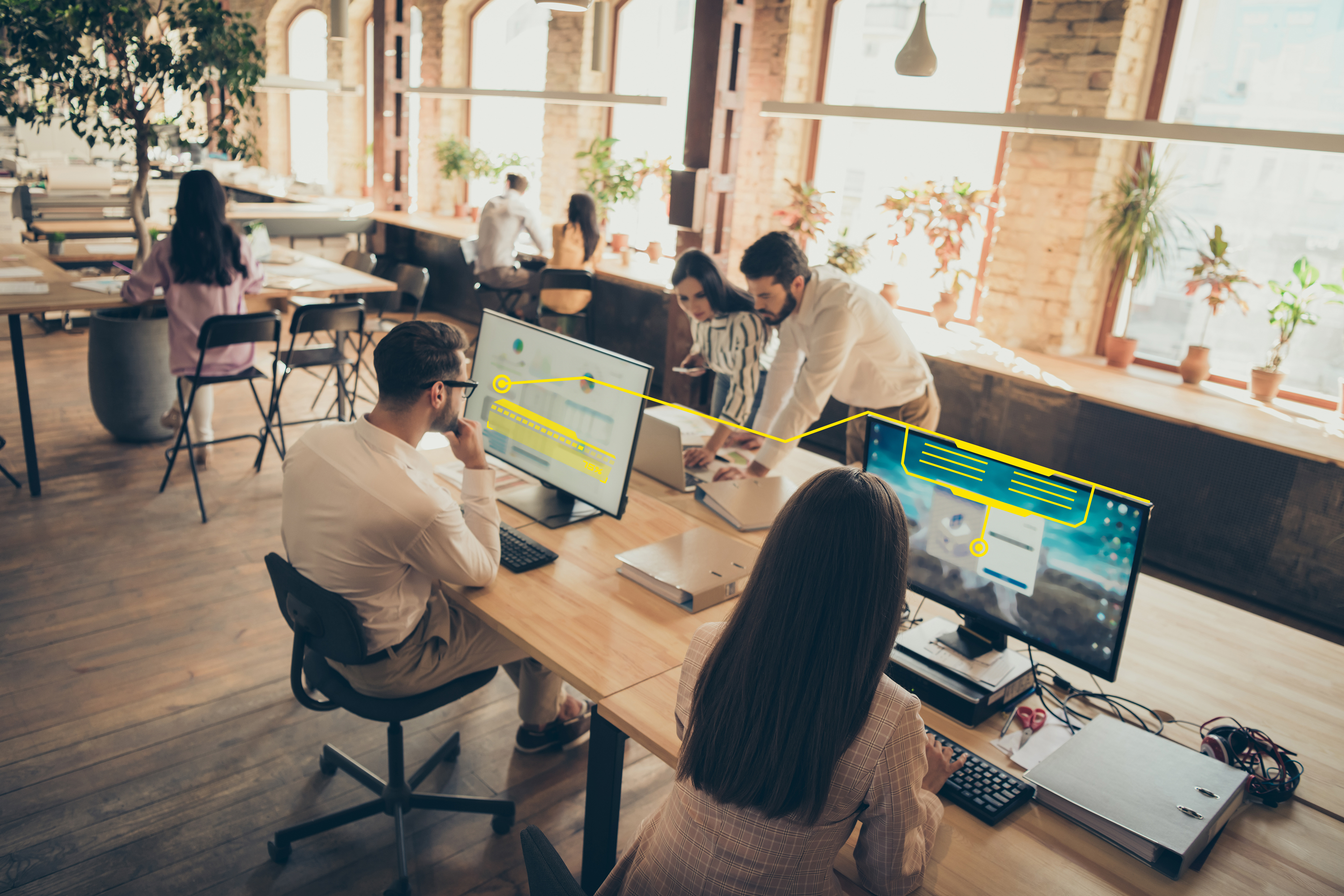 Professionals working together in an open office, analyzing data and digital insights displayed on desktop monitors.
