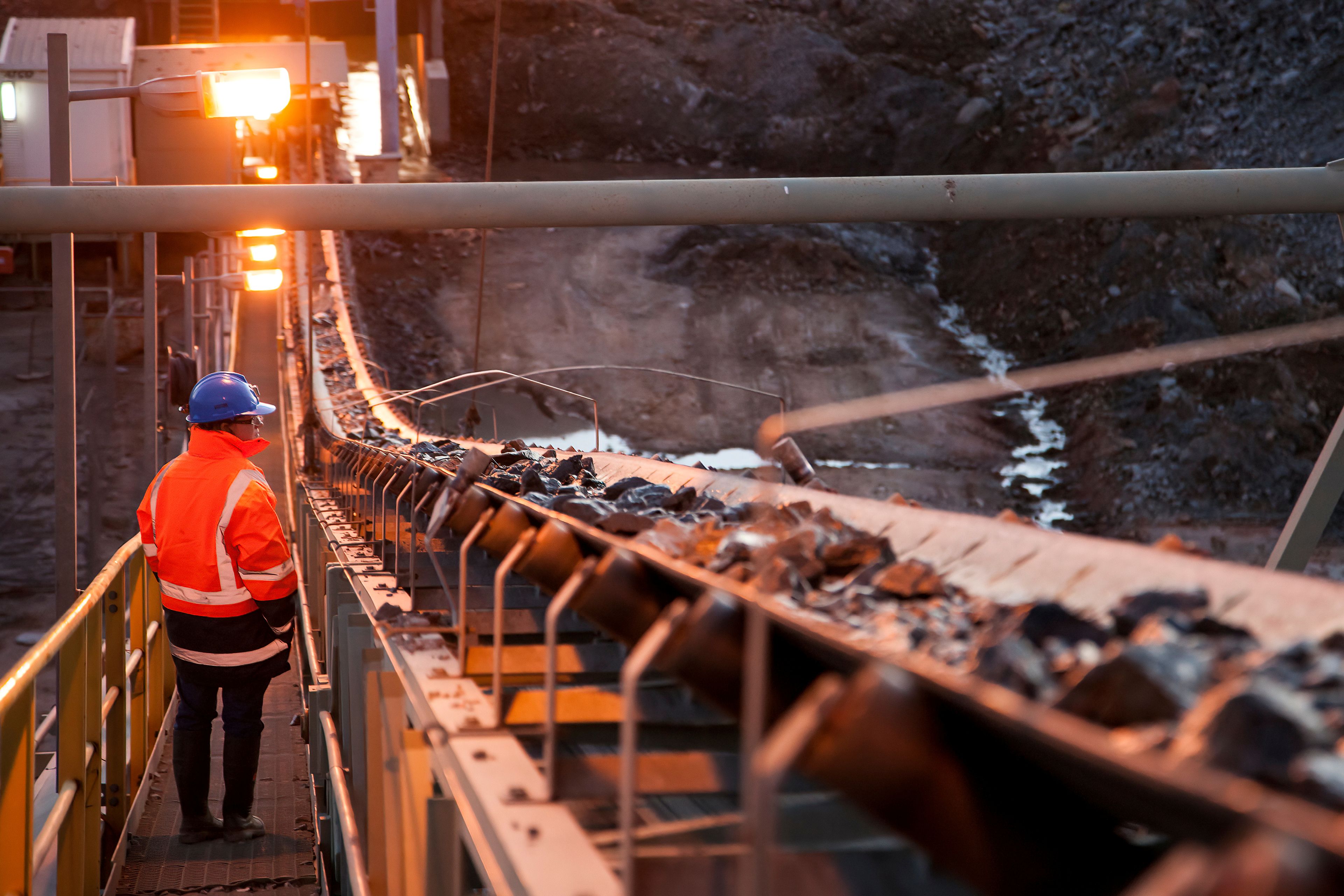 Worker inspecting a mining conveyor belt during operations