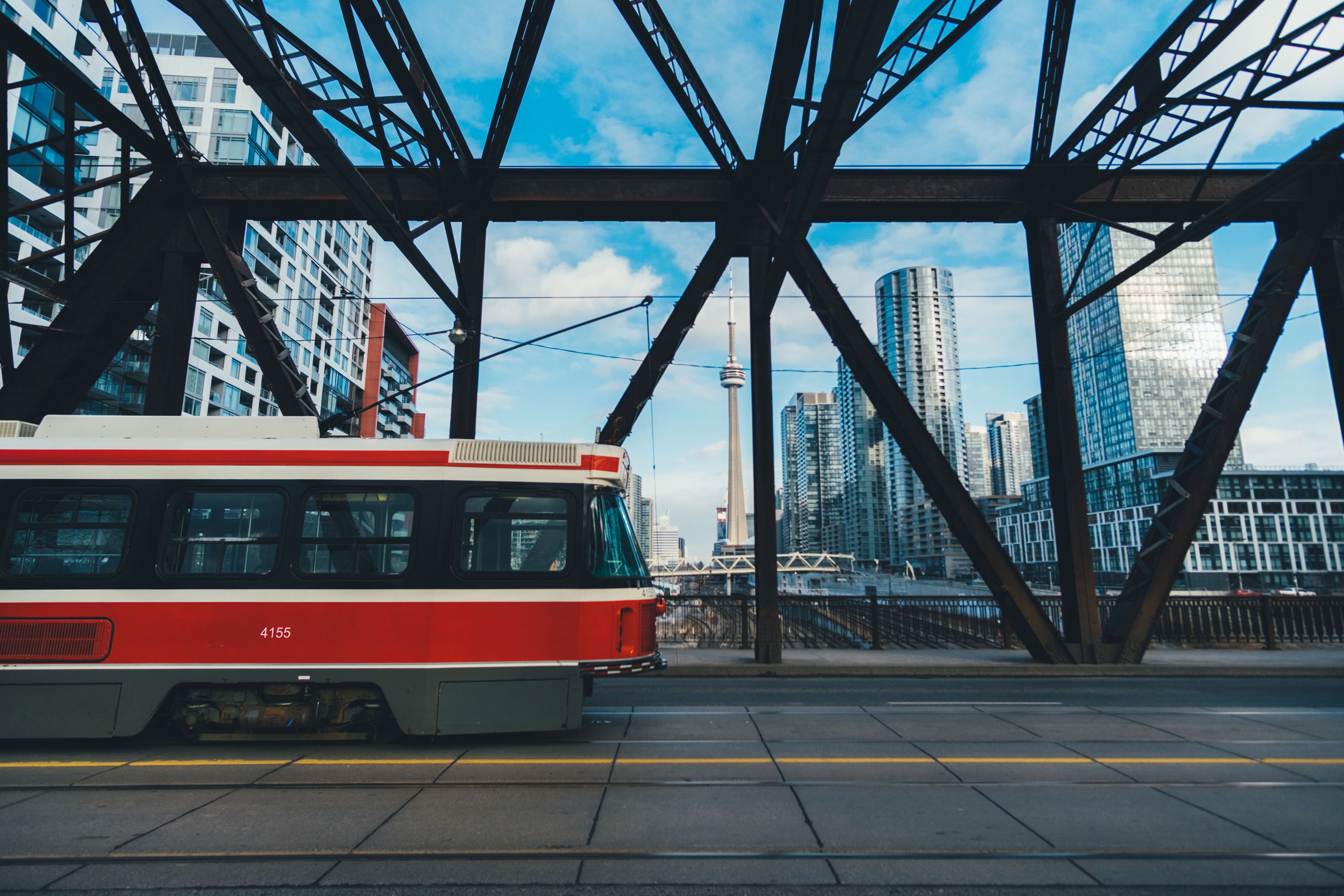 Red train crossing a steel bridge with modern city buildings in the background