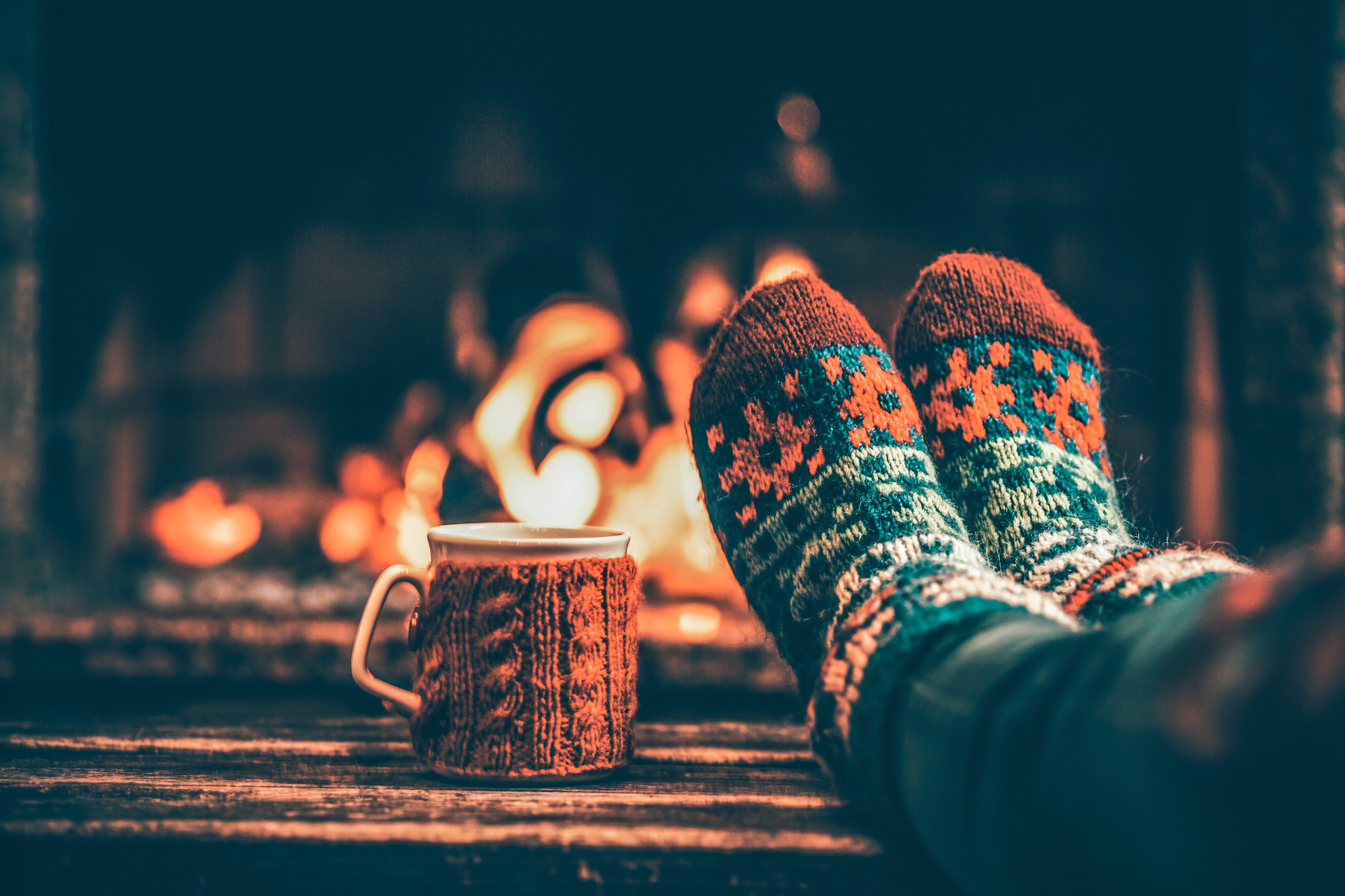 Warm patterned socks and a hot drink beside a fireplace