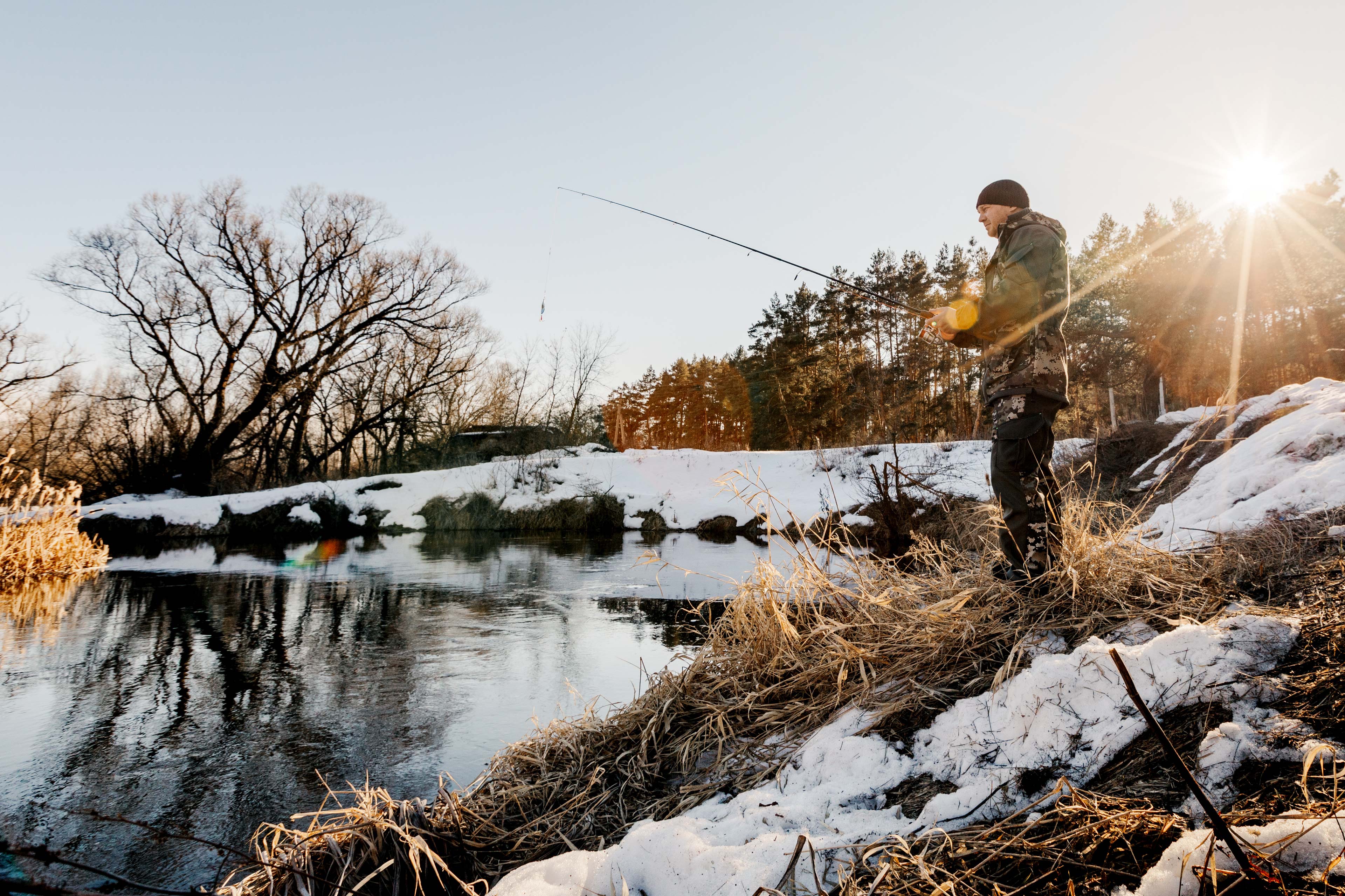Person fly fishing along a snowy riverbank