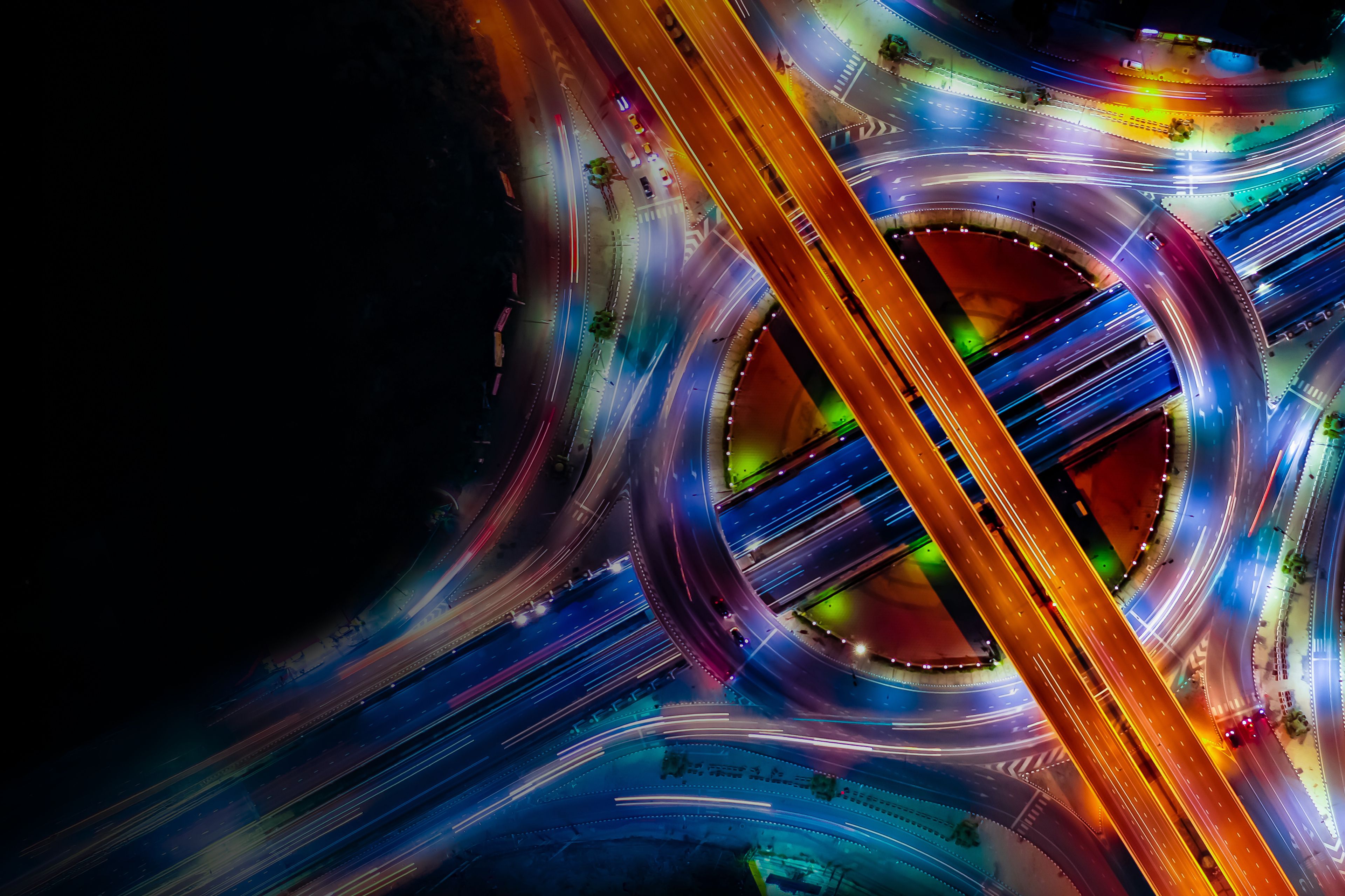 Colorful aerial view of a busy highway interchange at night with glowing traffic light trails.