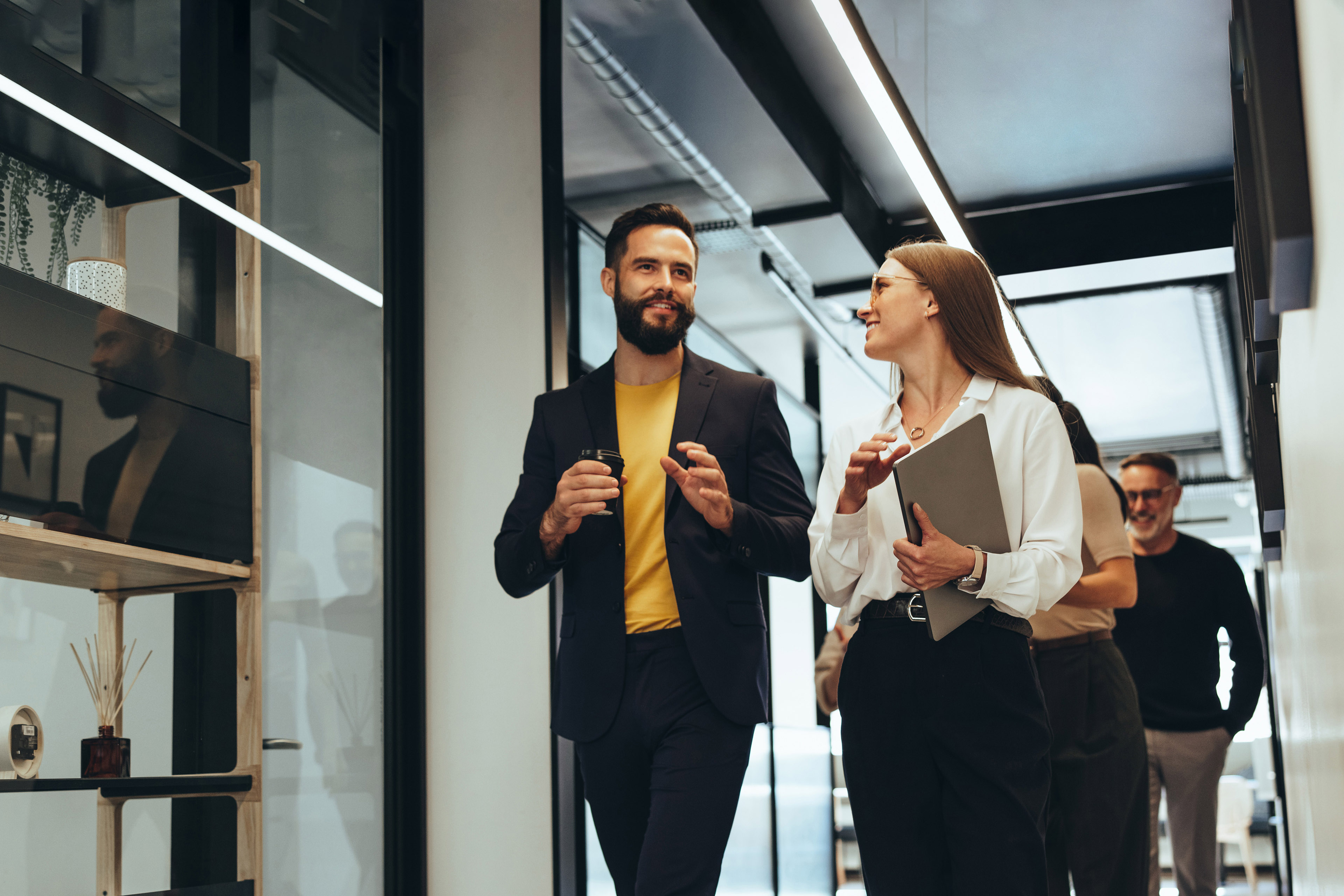 Two happy young businesspeople smiling while walking together in a hallway. 