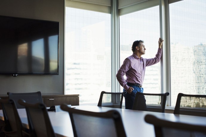 Man in a meeting room looking out of a window at urban landscape