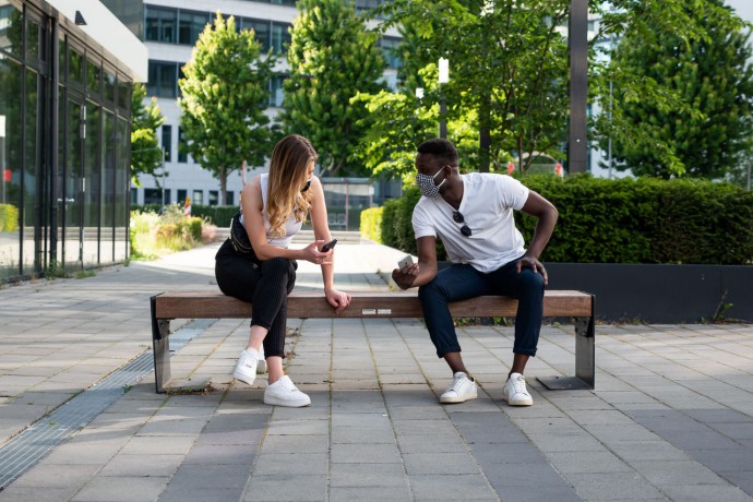 Young man and woman social distancing on bench using phones