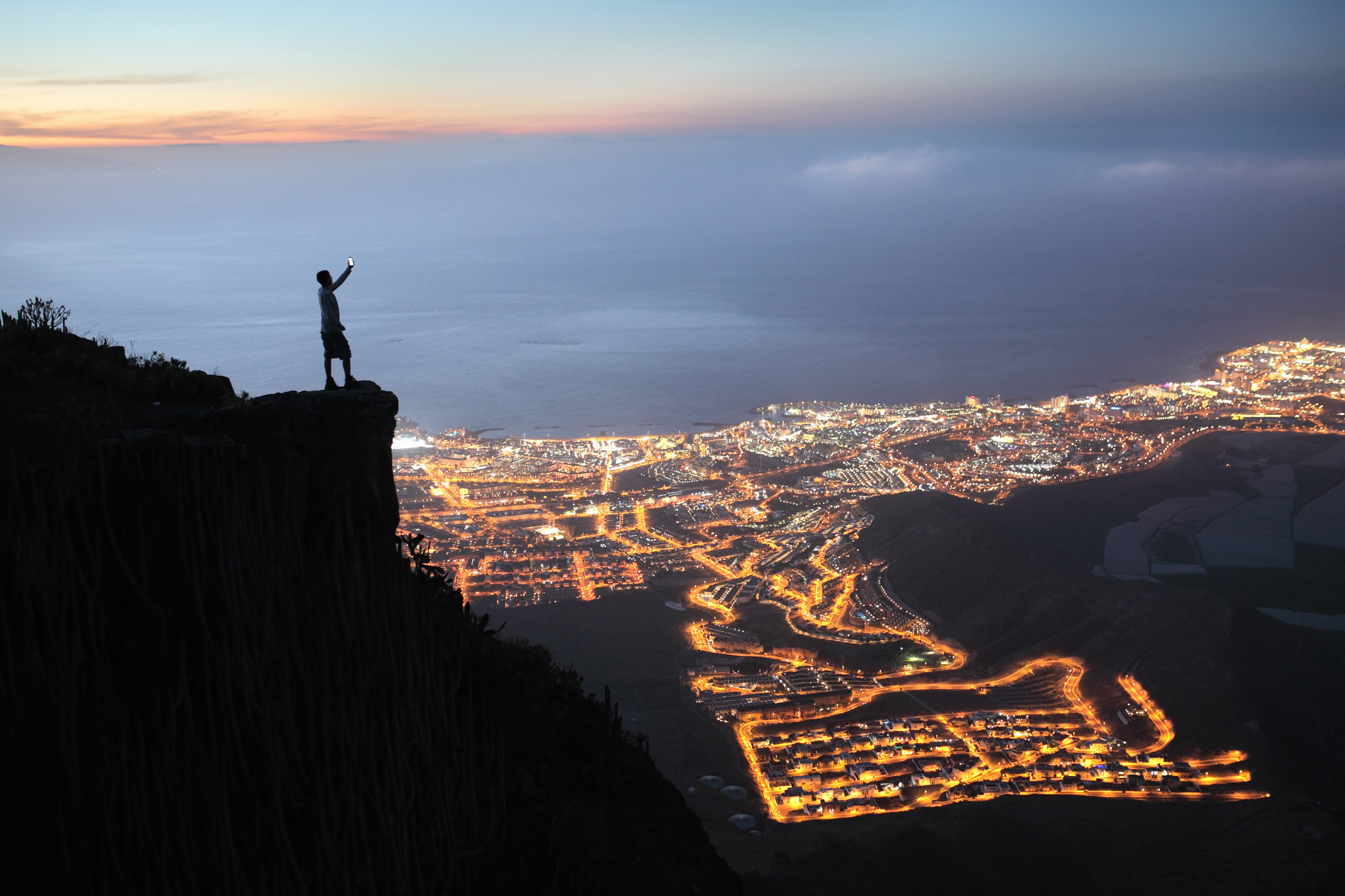 man with mobile device overlooking city at night.