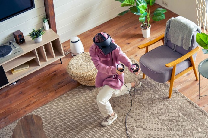 A photograph of a teenager girl wearing a vr headset and playing a virtual reality game at home.