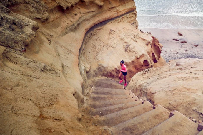 A photograph of a teenage girl running up steps by a beach