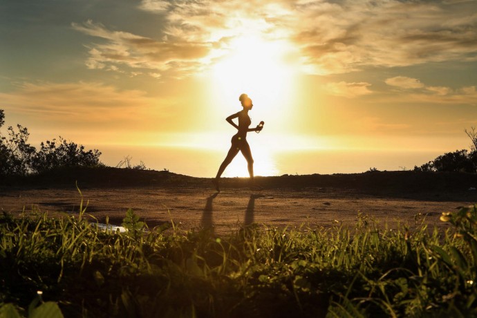 Woman trail running with sun behind her background