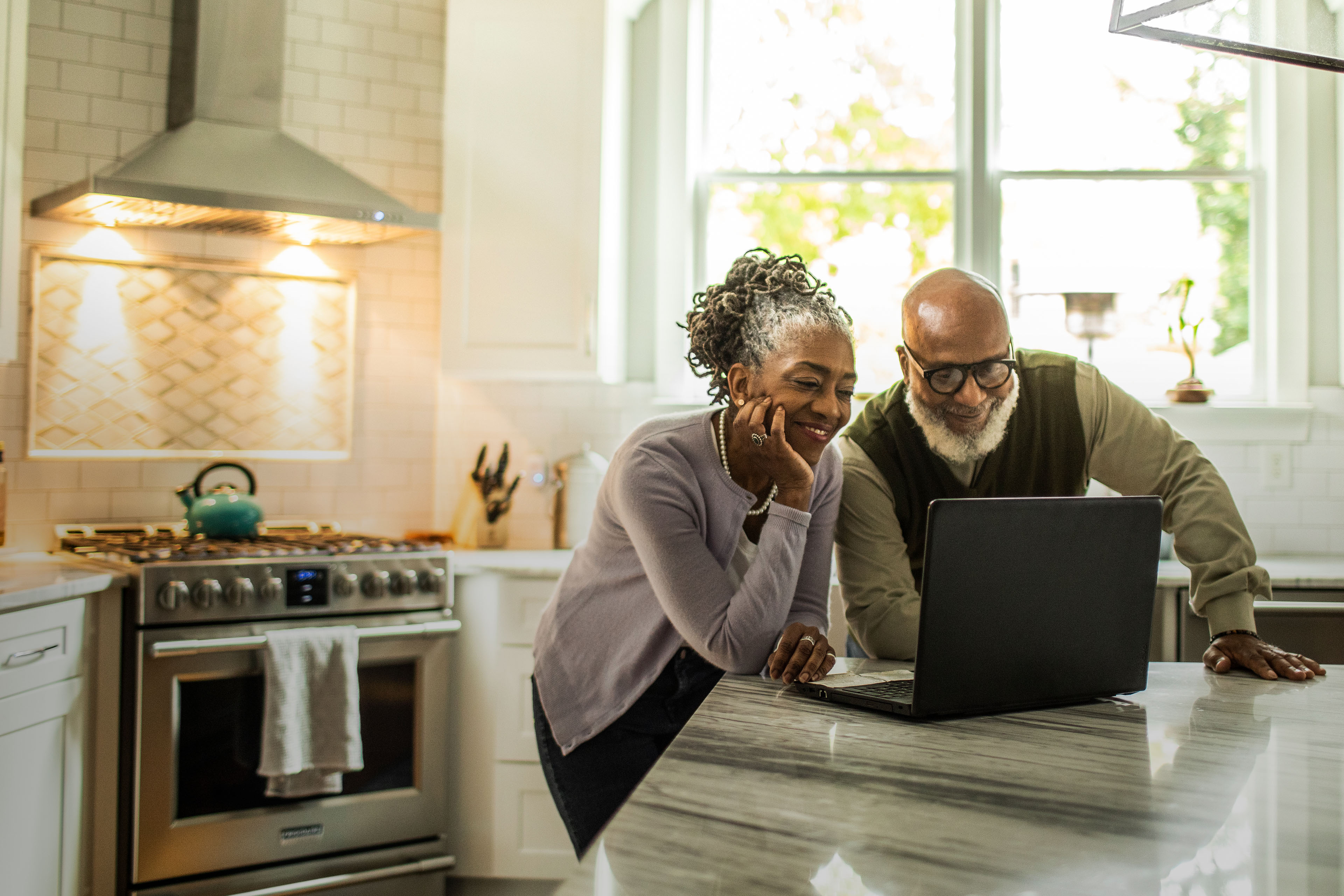 Senior couple using laptop in kitchen of suburban home