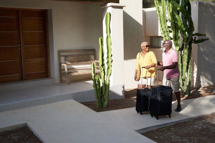 Mature couple walk luggage up the entrance of a luxury villa