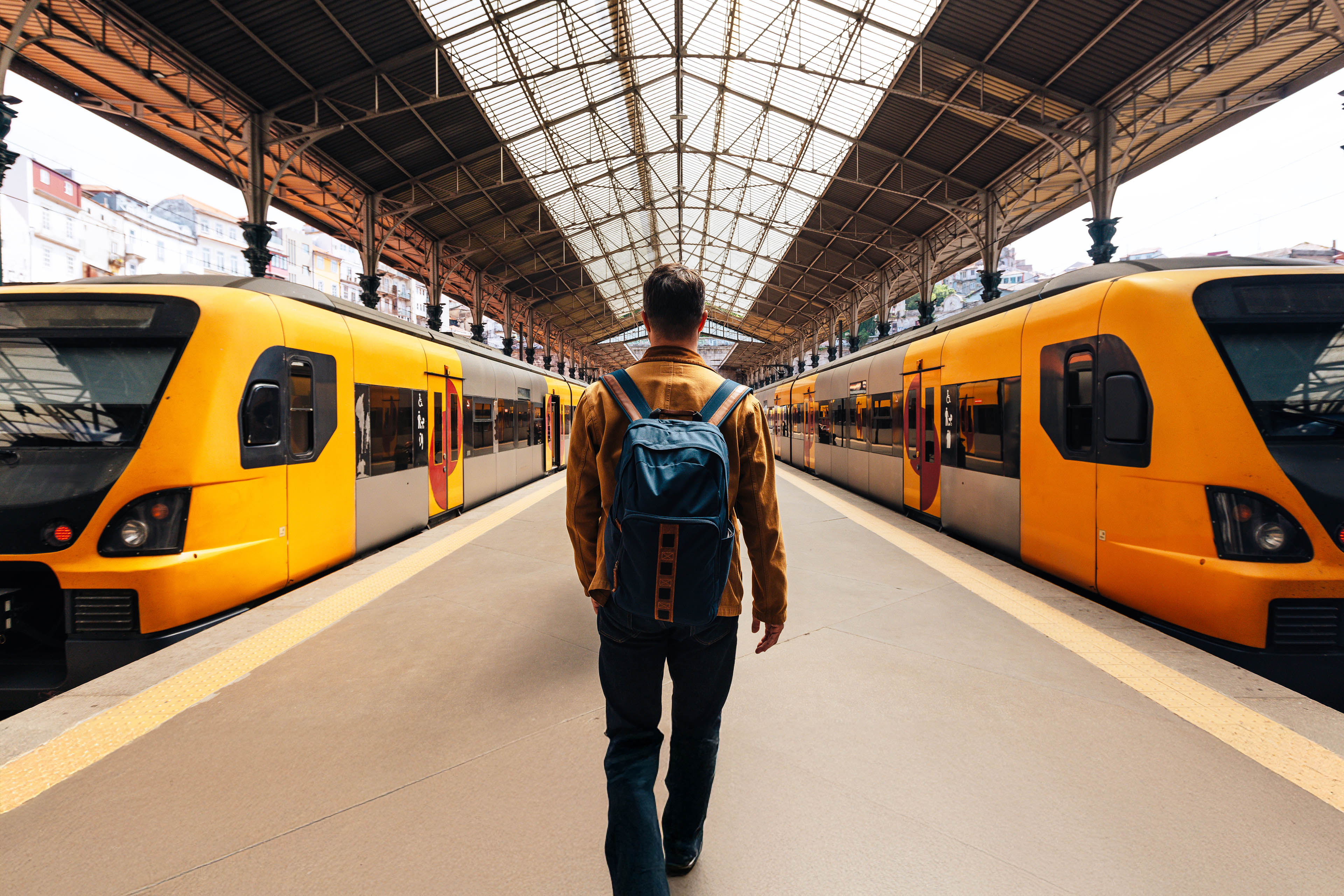 Rear view of a man with backpack walking between trains on train station