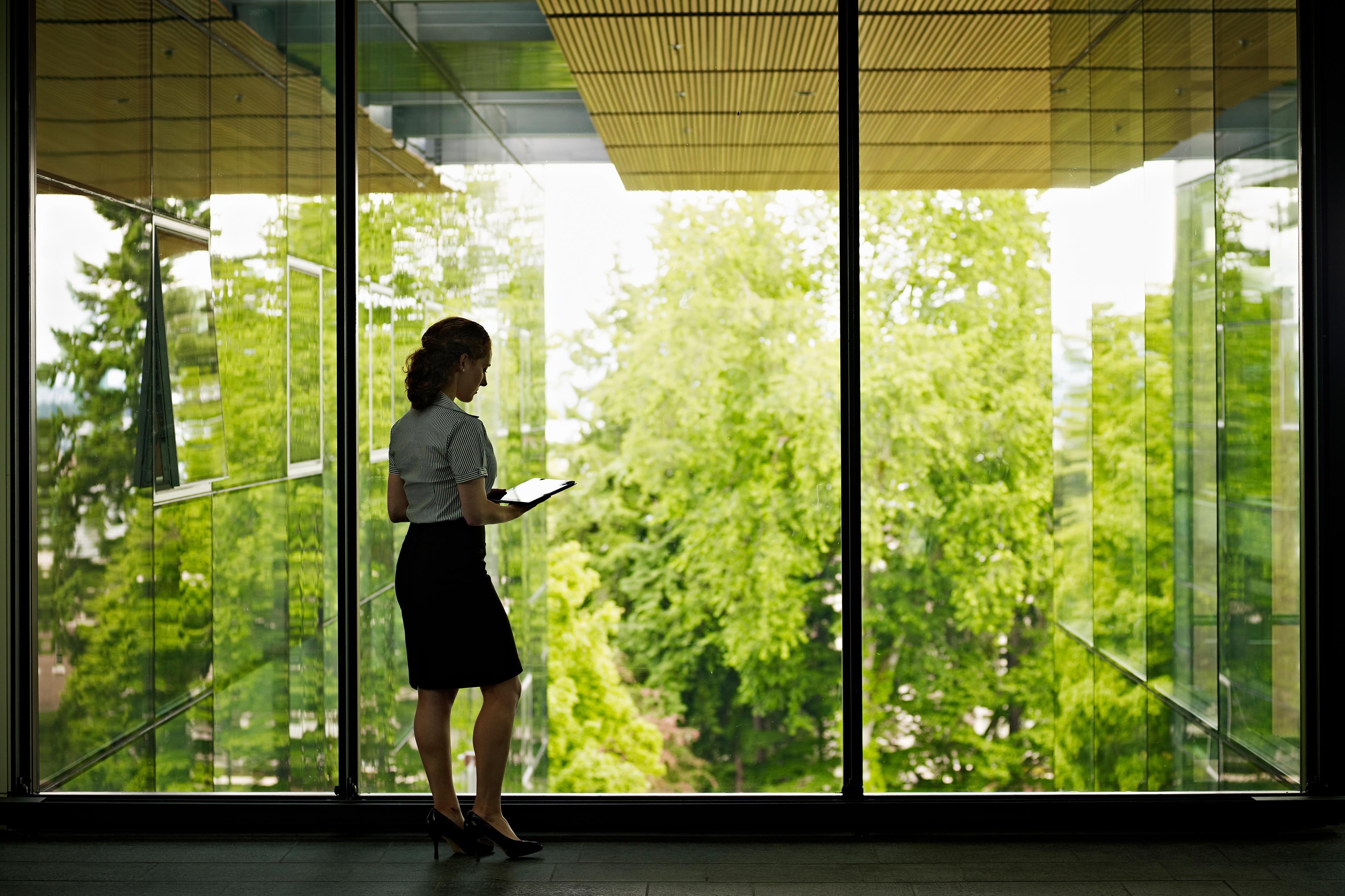 Businesswomen holding tablet standing at windows looking green nature