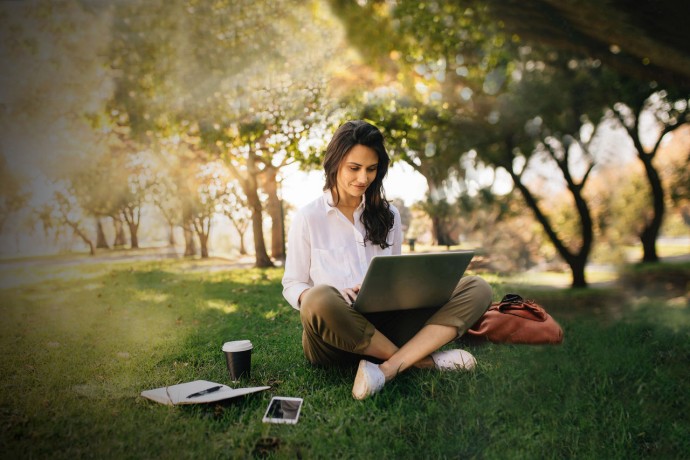 Freelancer working on laptop on green lawn in park background