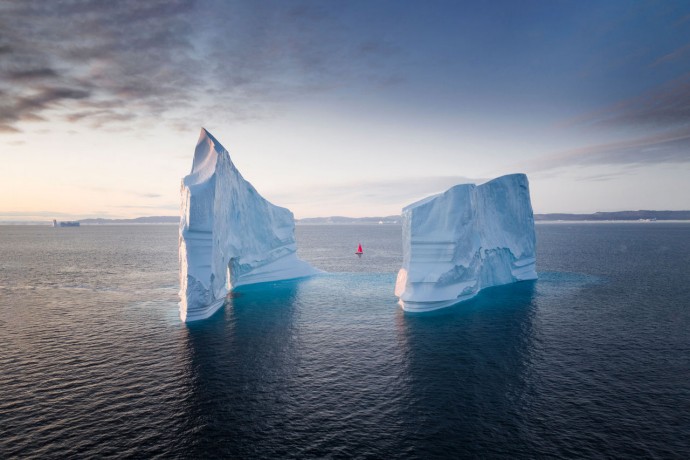 Boat with red sail between icebergs in Greenland