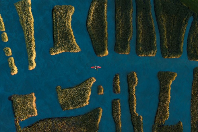 aerial shot of kayak navigating between grassy patches of lan