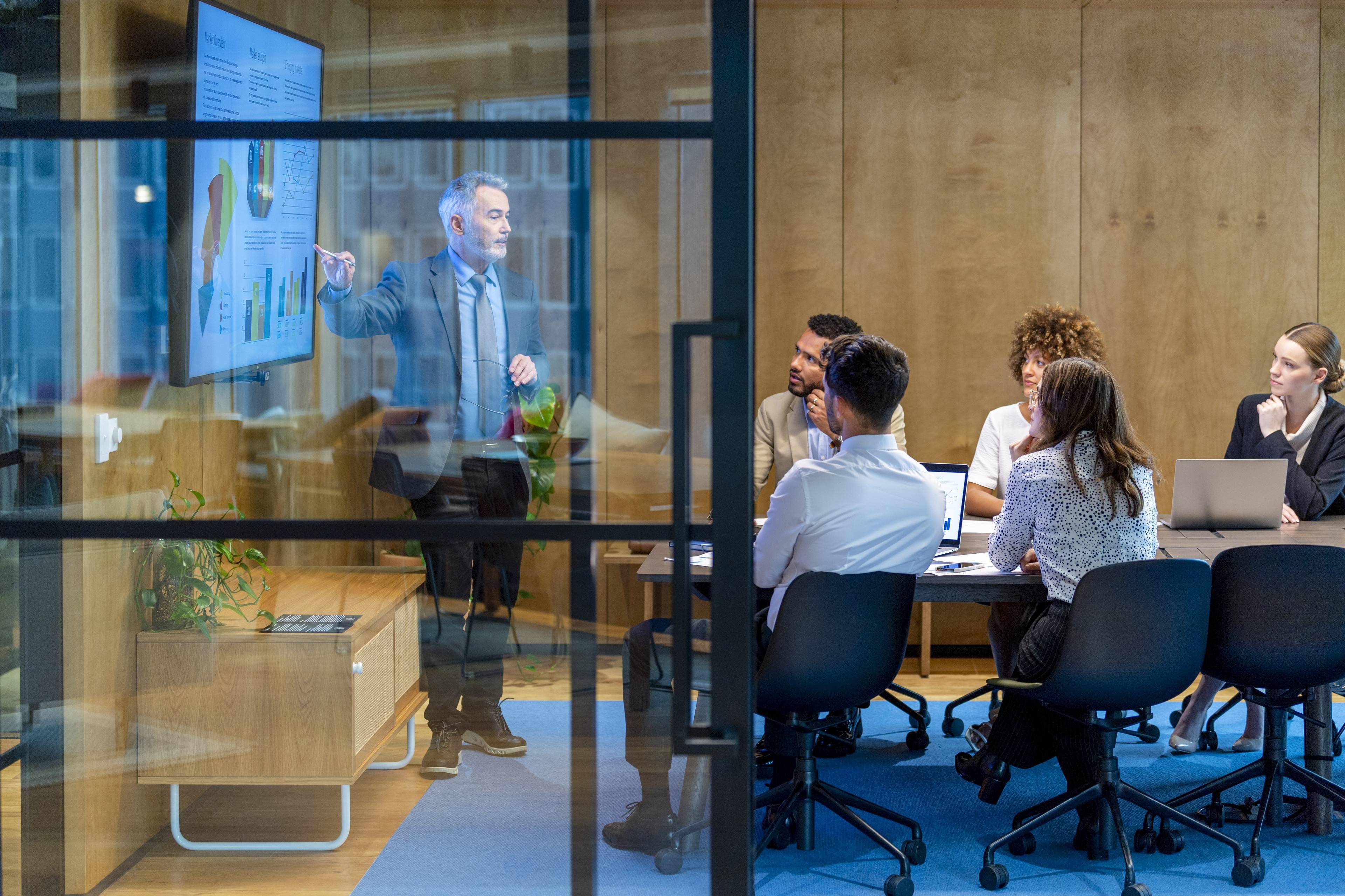 Mature man giving a big data presentation on a tv in a board room.
