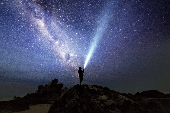 Man on rocks with flashlight and the milkyway