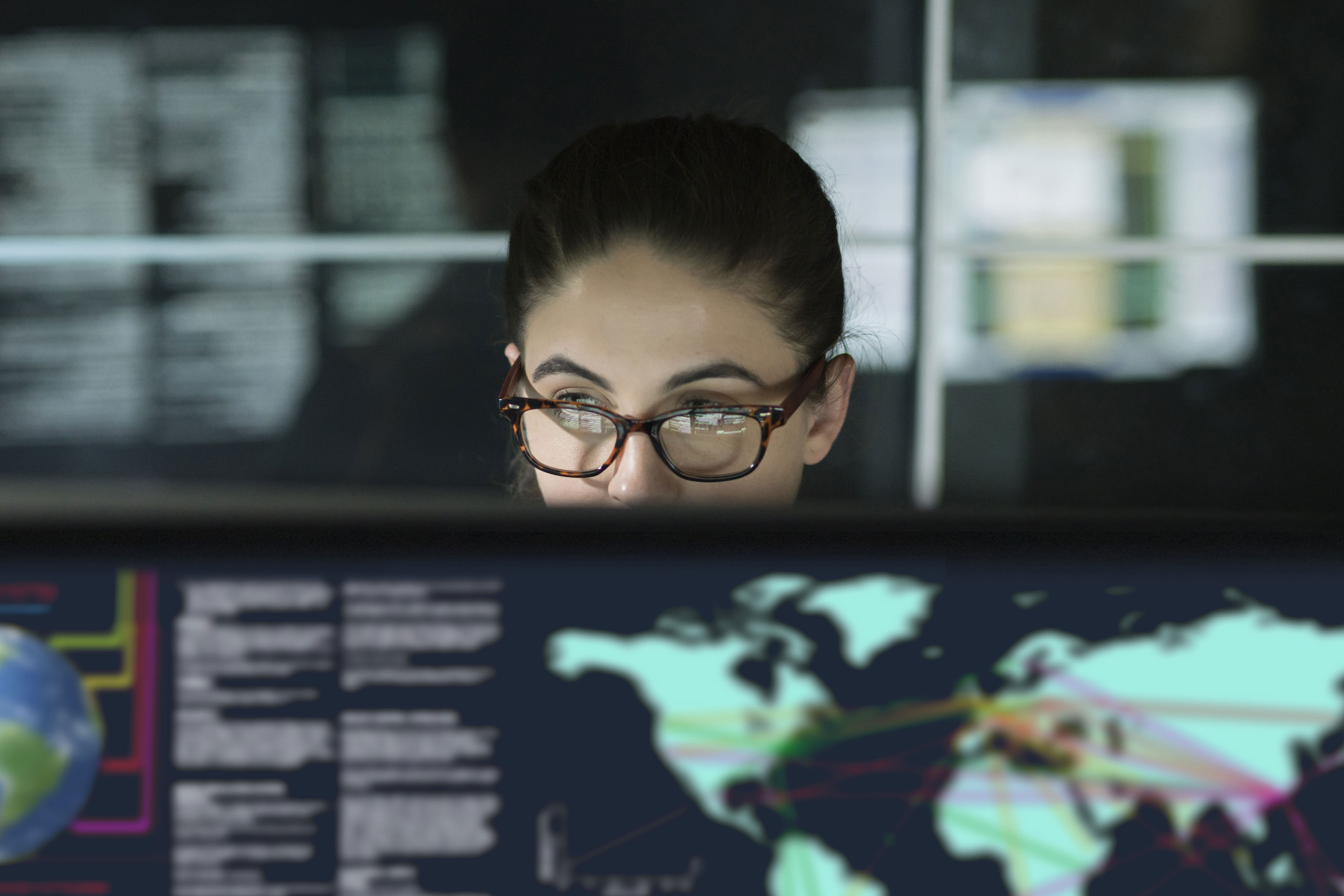 Young woman, surrounded by computer monitors in a dark office.