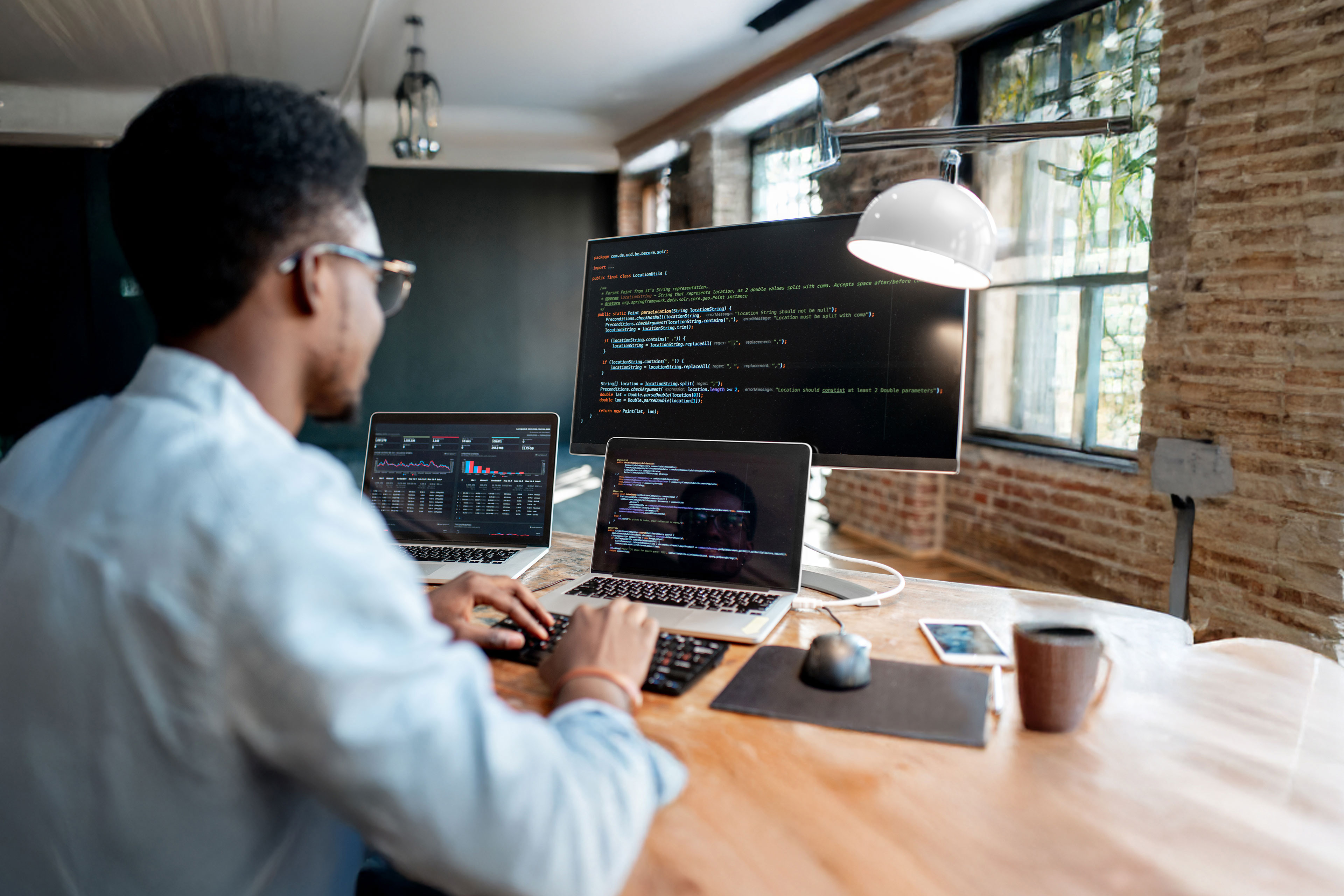 Young male programmer writing program code sitting at the workplace