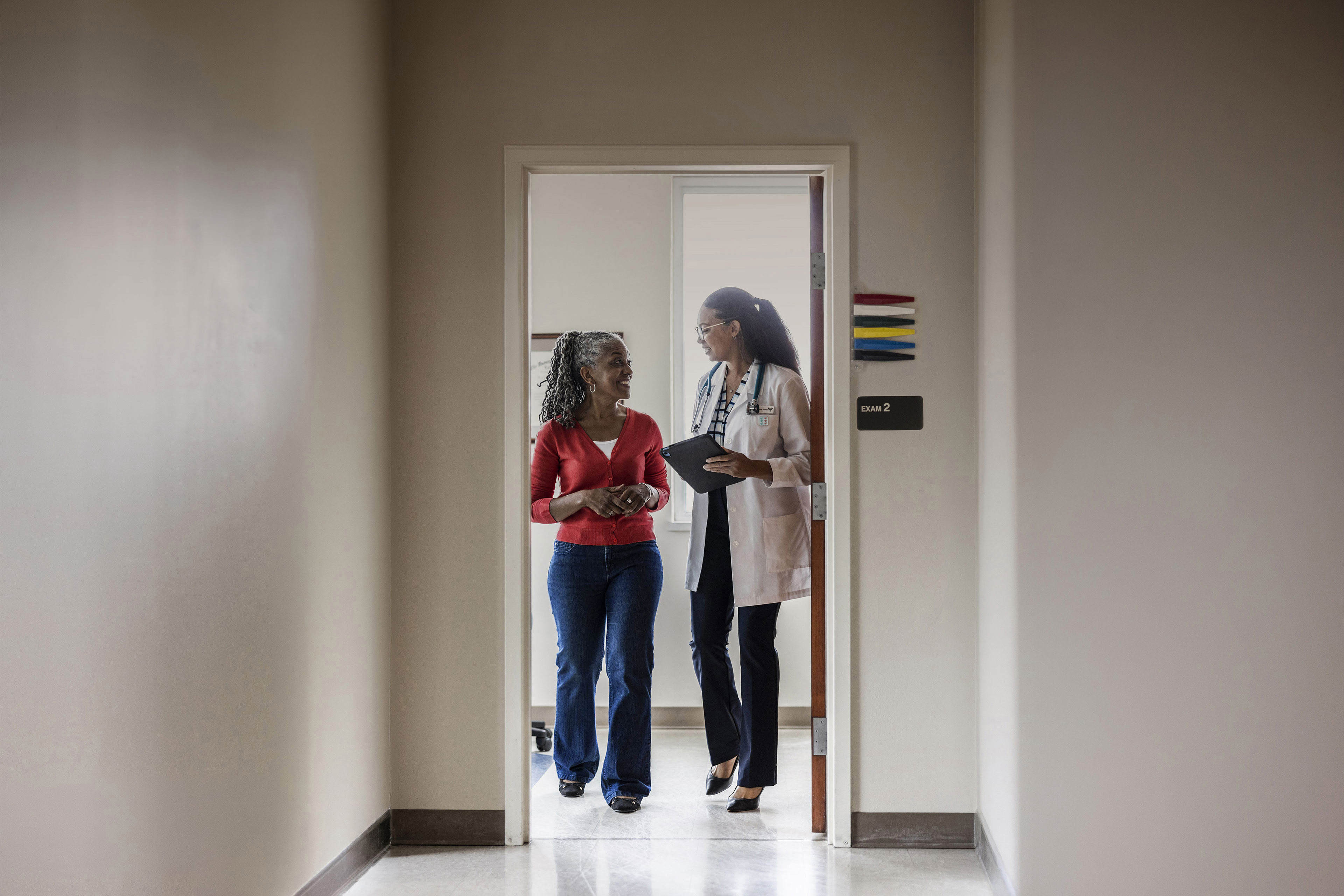 Healthcare professional and patient discuss care and treatment options while walking through a medical facility corridor