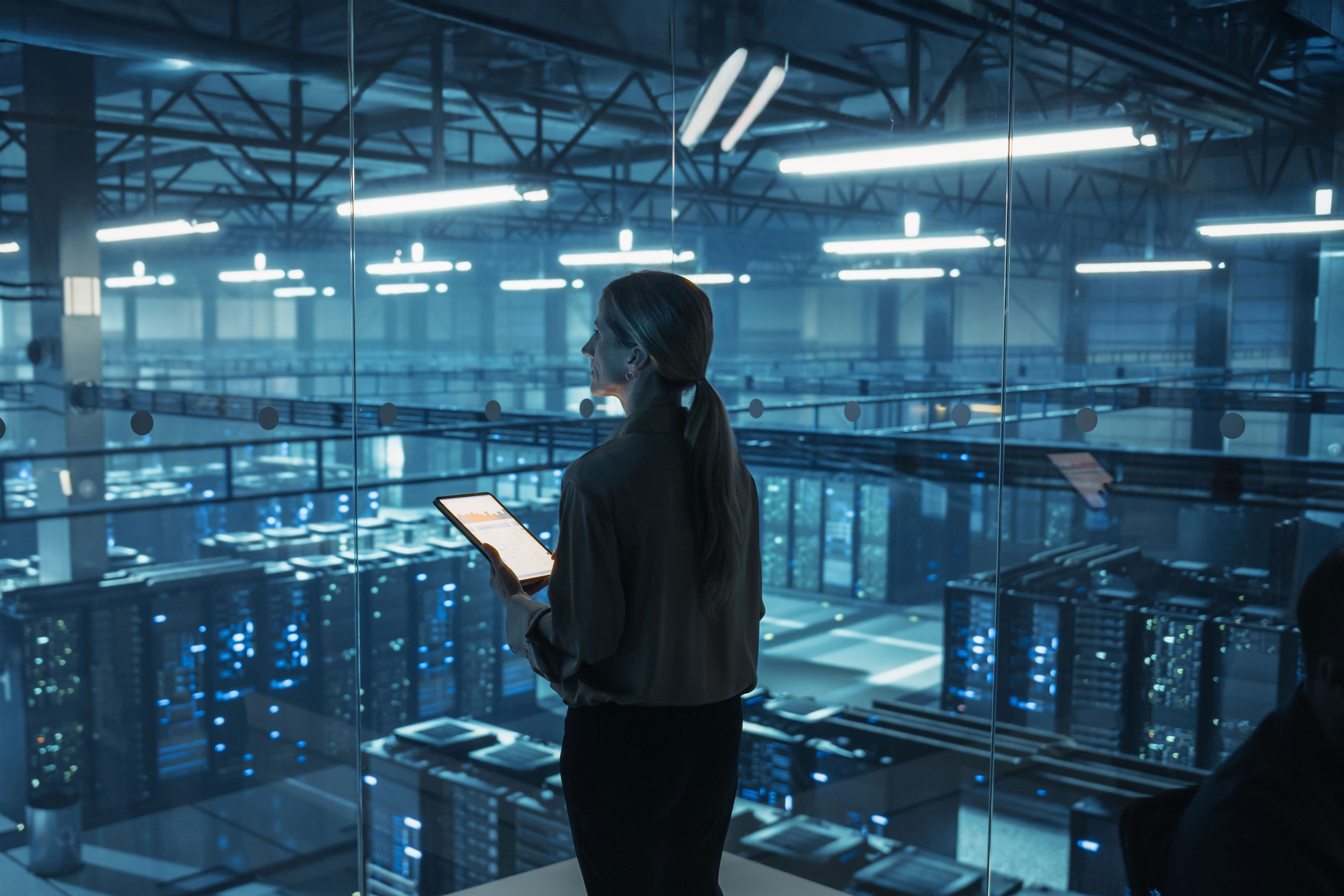 Female IT engineer reviews security logs on a tablet in a data center to identify risks and ensure network security.