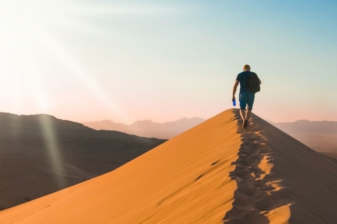Man walking up desert hill with water bottle
