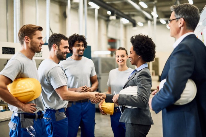 Happy businesswoman shaking hands with worker while visiting factory