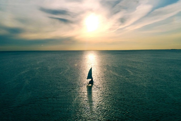 Sailboat floating on the water towards the horizon in the rays of the setting sun