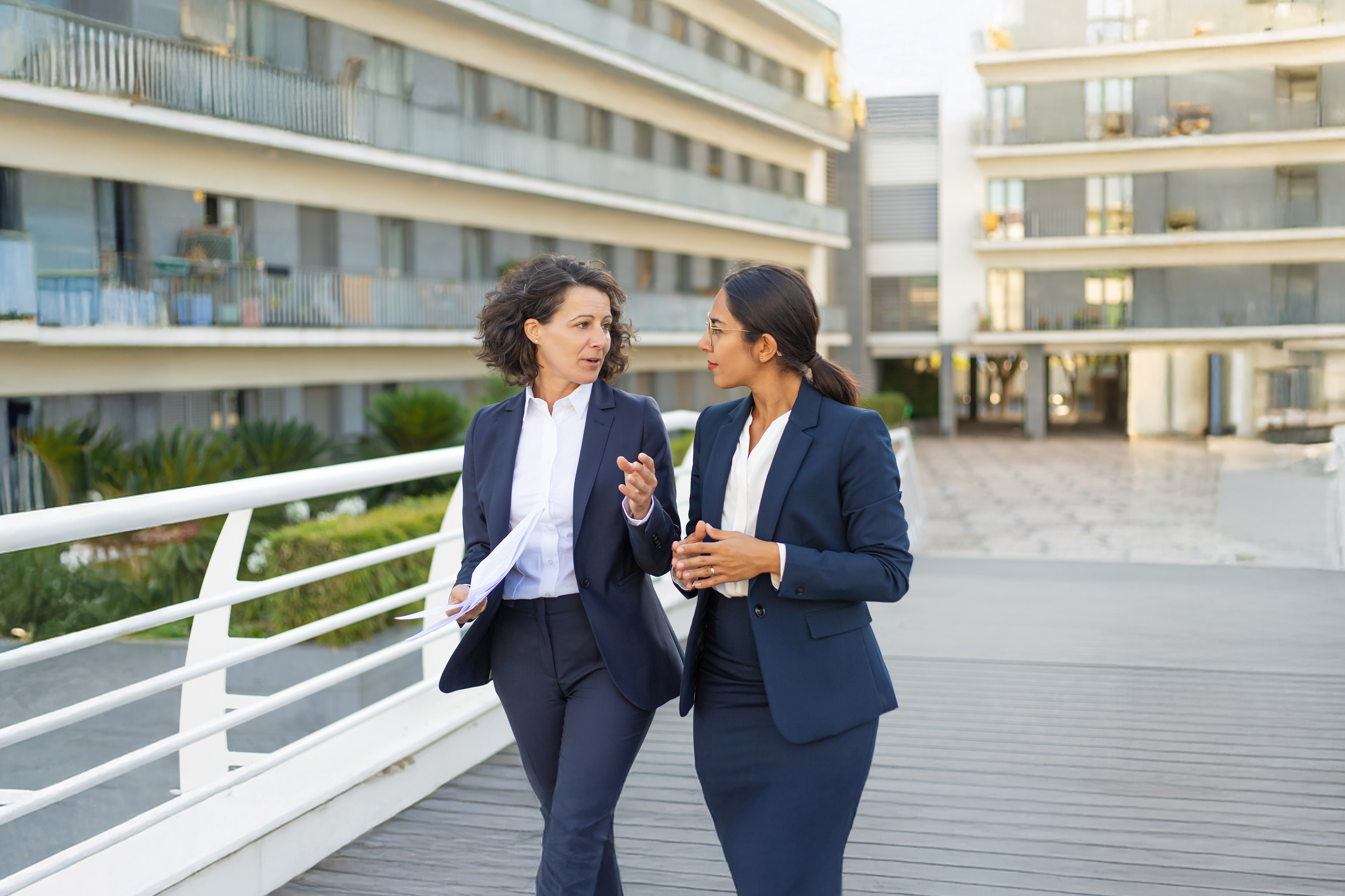 Focused female professionals discussing project on their way to office. Business women walking outside in city.
