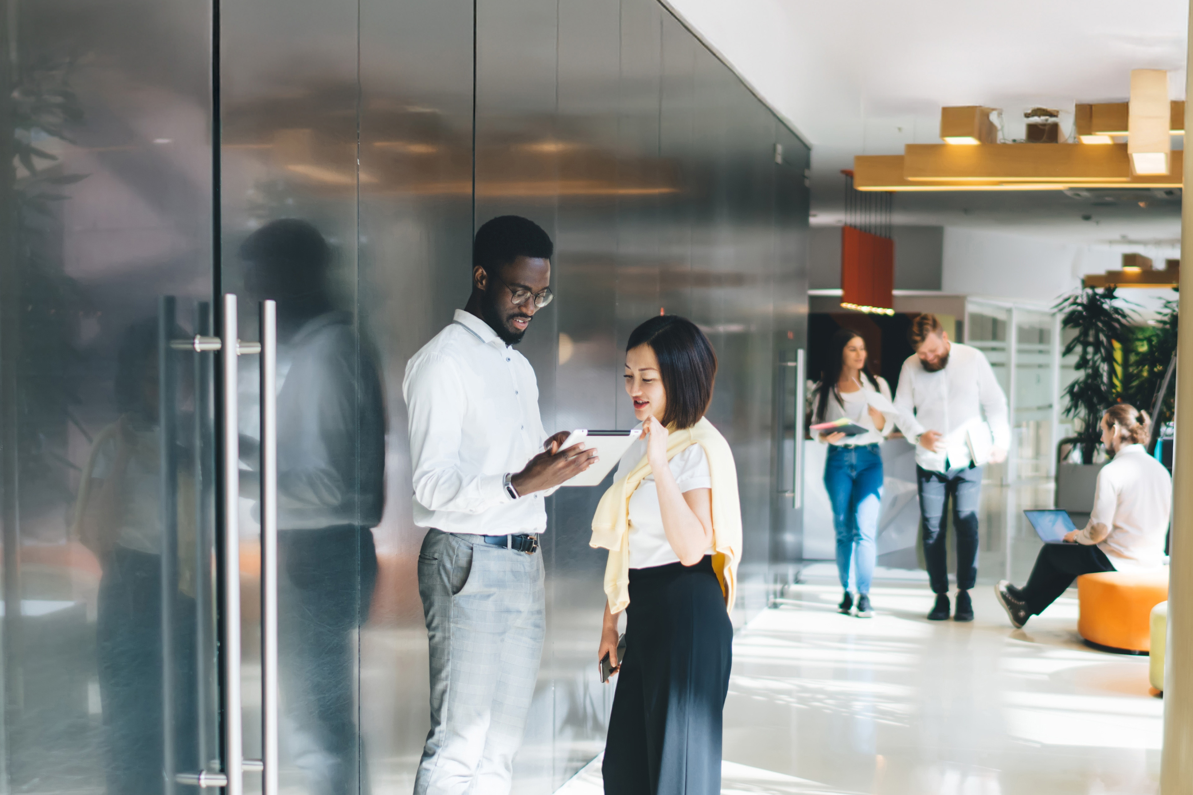 Multiethnic staff in casual clothes walking and standing in big sunlit corridor of modern workspace.