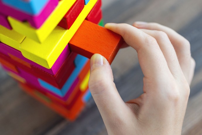 Close up of a hand pulling a colorful jenga block from a big pile