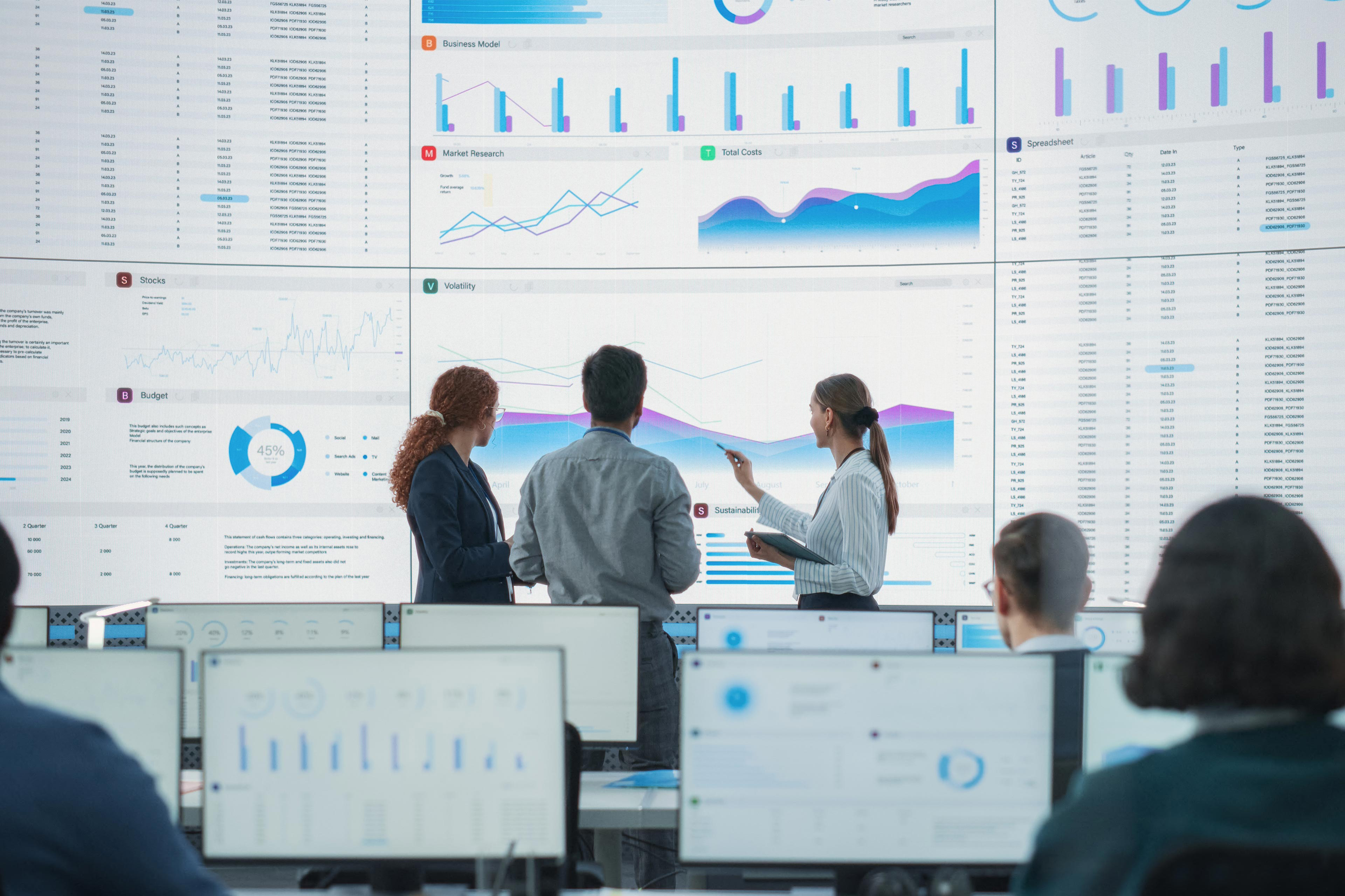 Wide Back Shot of Diverse Team of Data Scientists Discussing Graphs And Reports On Big Digital Screen.