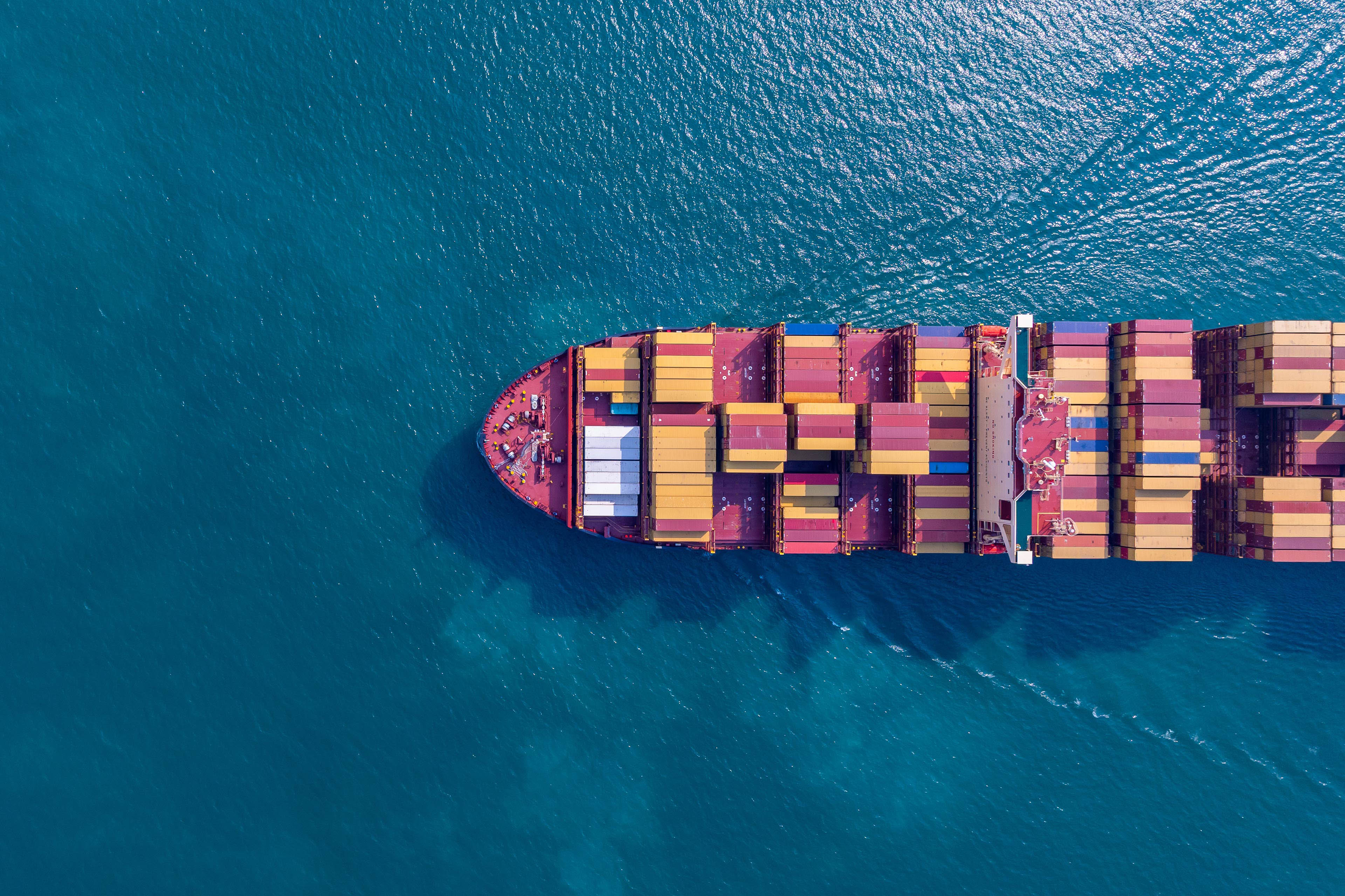 Aerial view of a container ship carrying freight across open waters, supporting global import and export logistics.