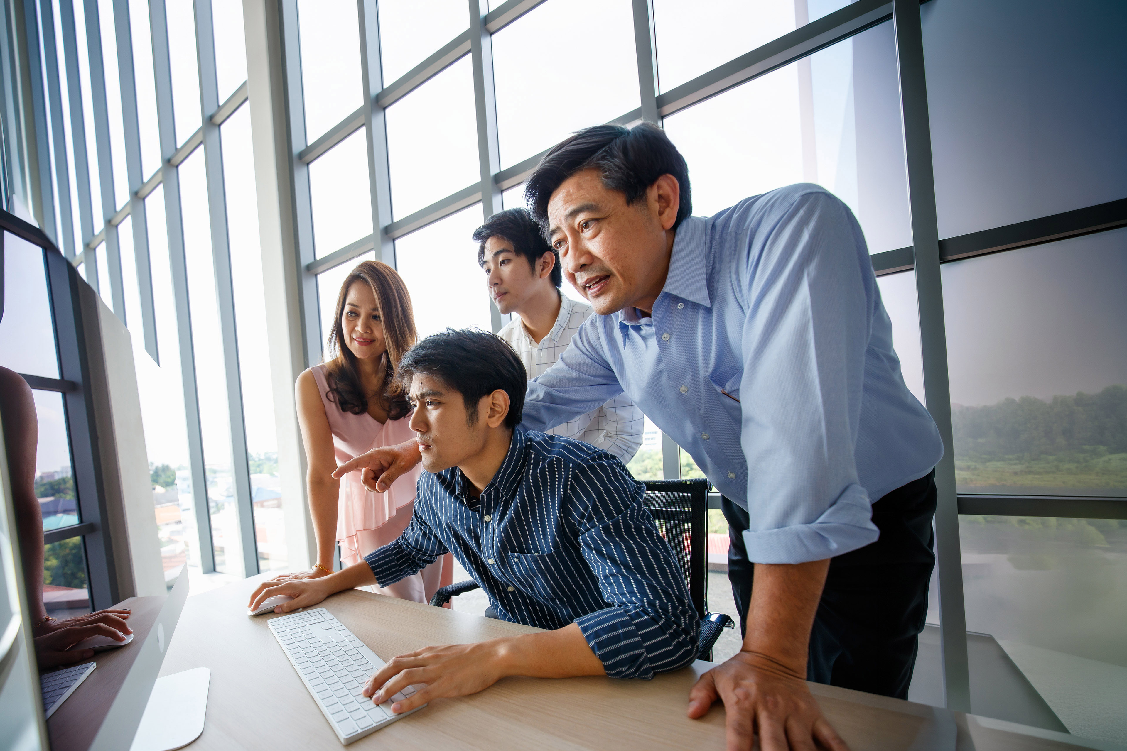 Asian family business team working on a computer in a modern office, smiling confidently and collaborating successfully.