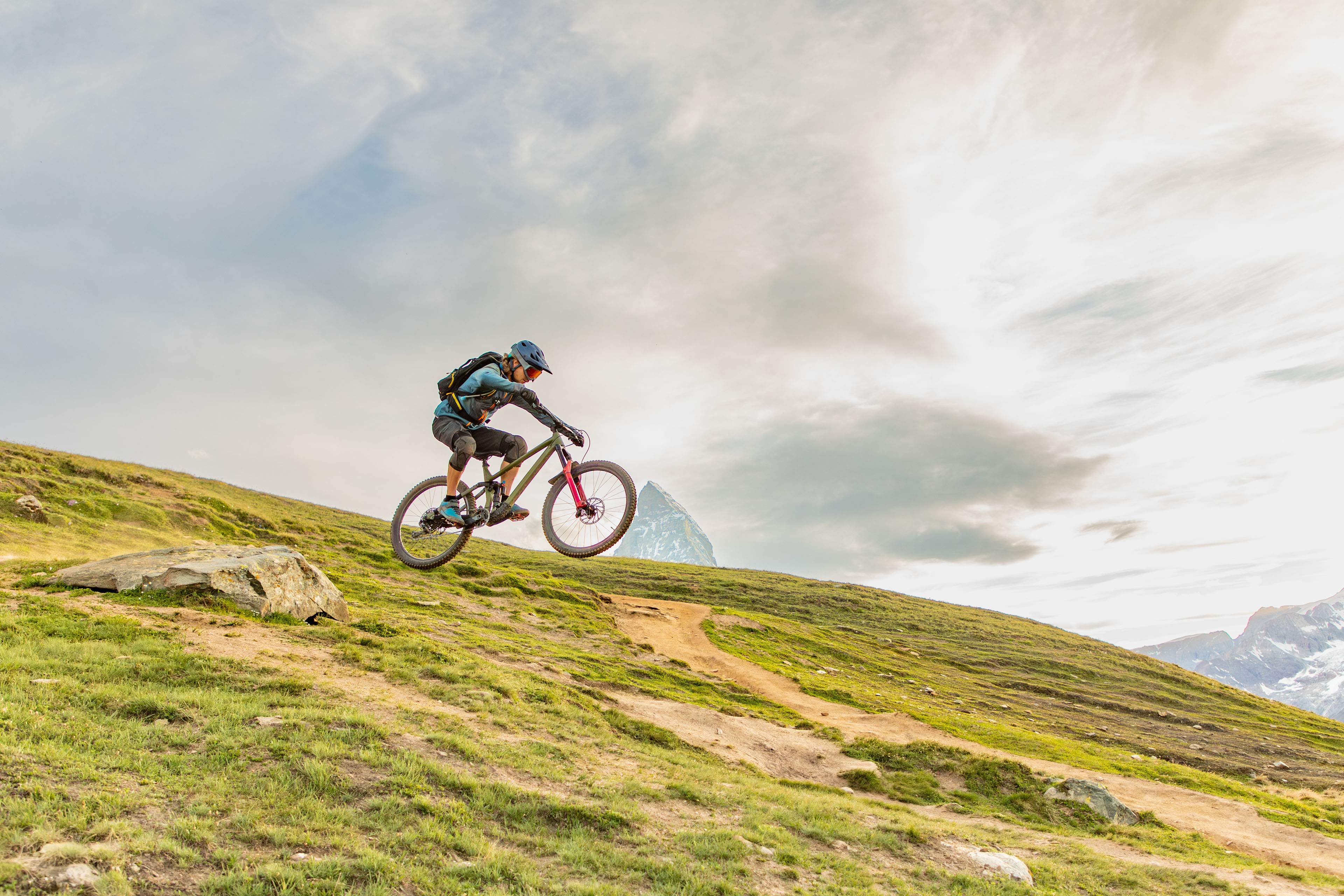 A man rides a mountain bike downhill in the Alps near Zermatt, with the Matterhorn behind, showcasing extreme thrills