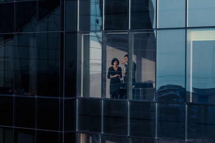 Aerial Shot From Outside of the Skyscraper: Businessman and Businesswoman Talking Business while Standing by the Office Window. Shot of the Financial Business District and Businesspeople Working in the Big City.