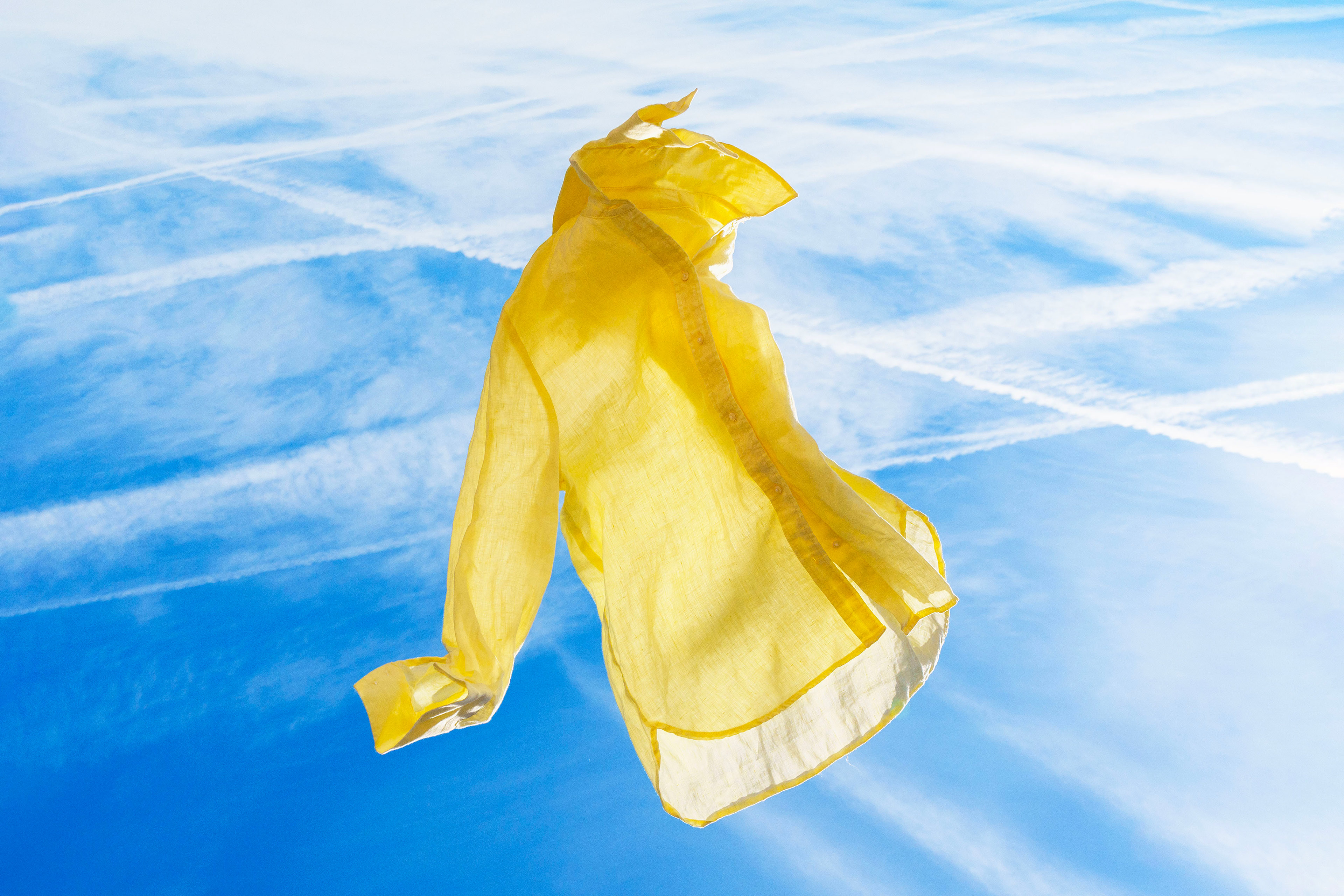Chemise jaune flottant dans un ciel bleu vif avec des traînées blanches