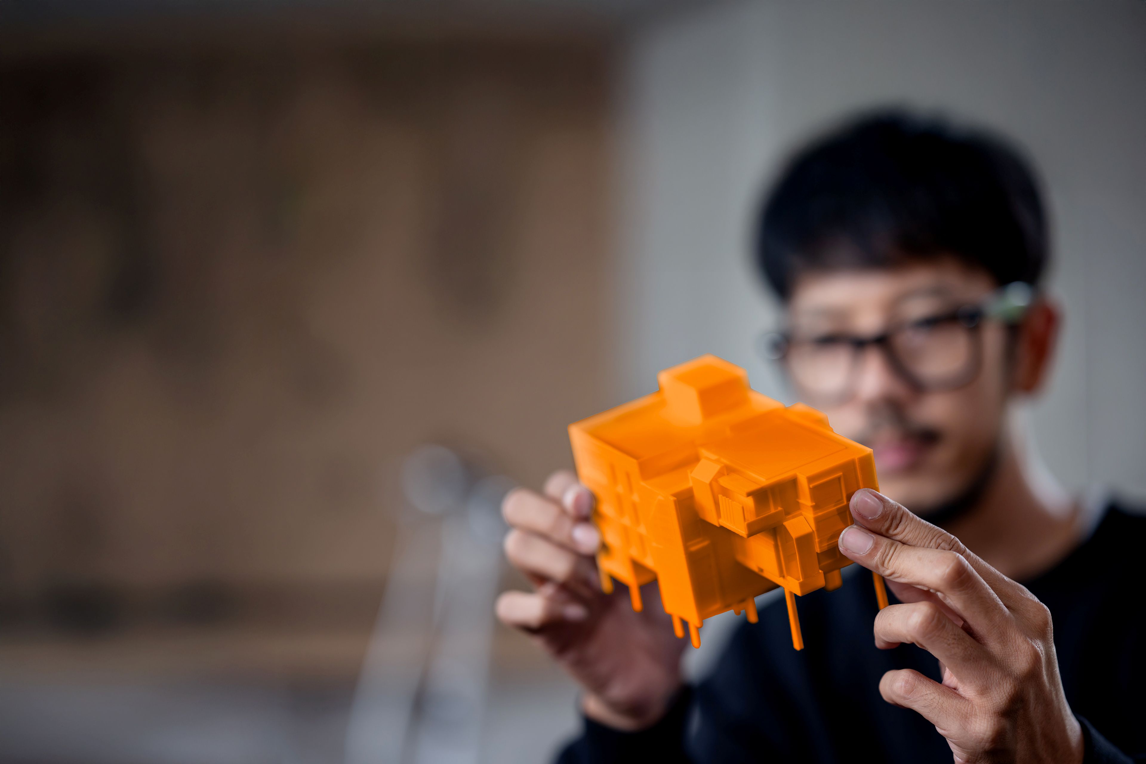 Une personne tient un petit modèle architectural orange et complexe.