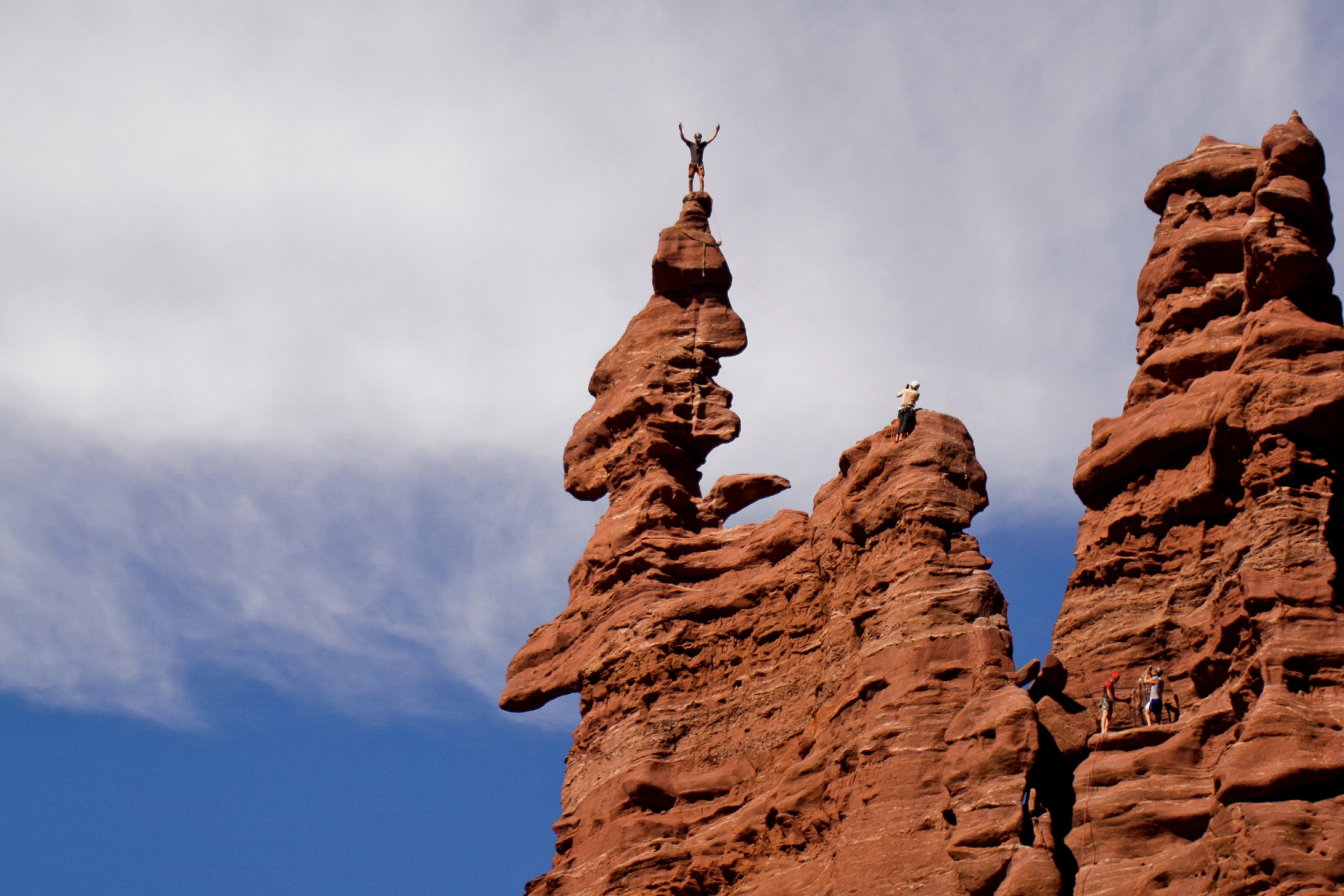 Personne debout au sommet d'une haute formation rocheuse rouge sous ciel bleu