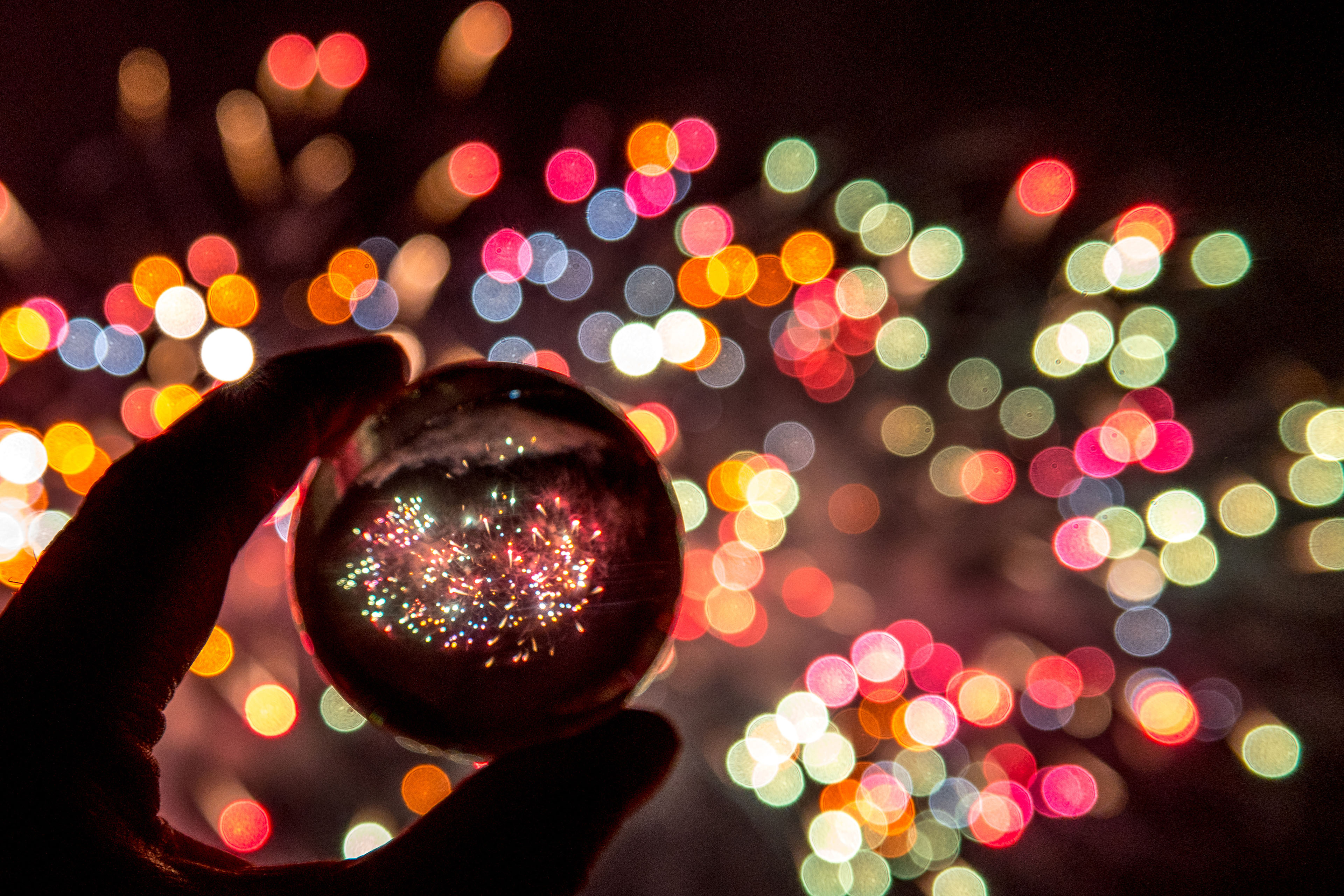 Une main tient une boule en cristal reflétant des feux d'artifice colorés.