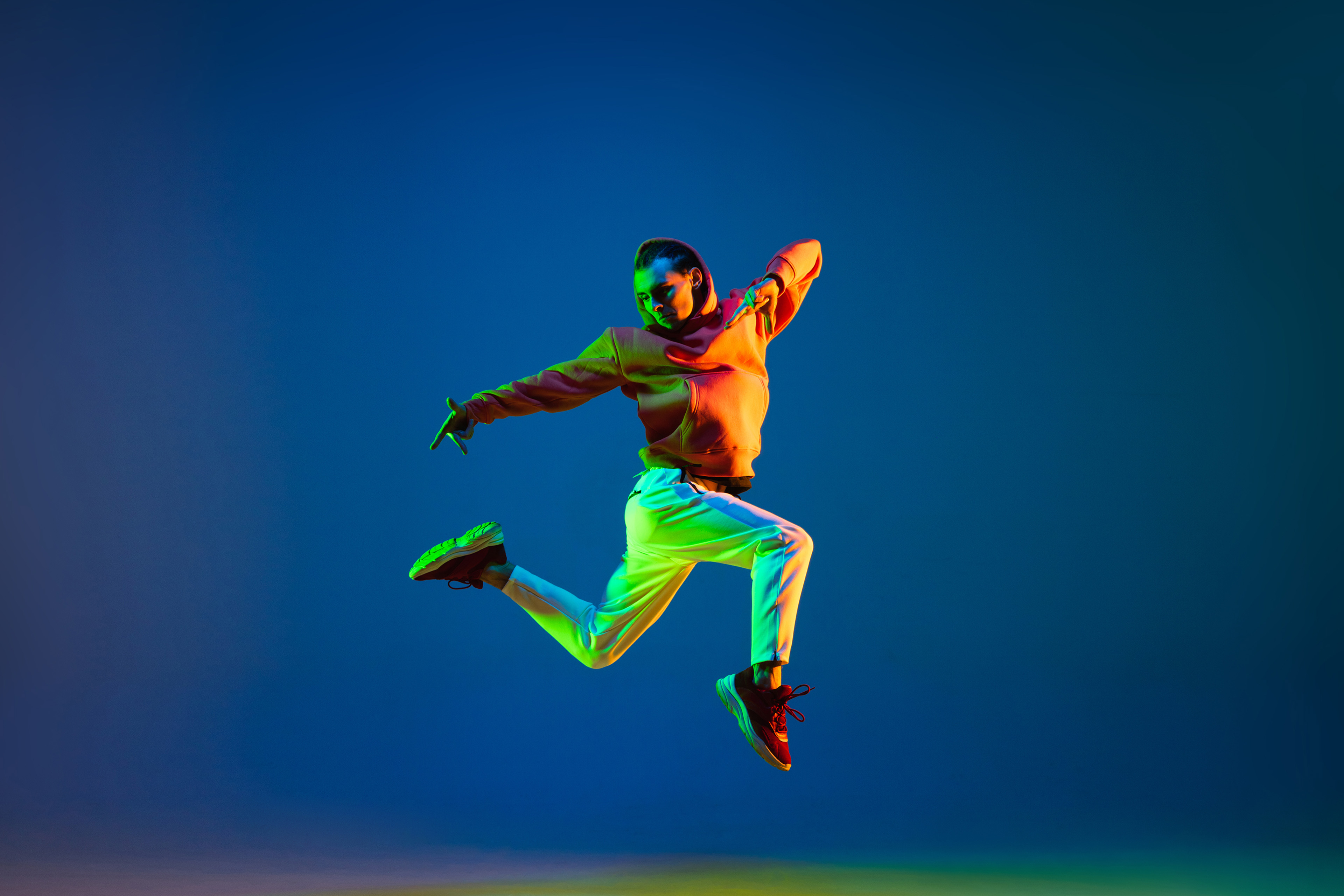 Danser in oranje hoodie in een dynamische dansbeweging, uitgelicht met fel groen, oranje en blauw licht