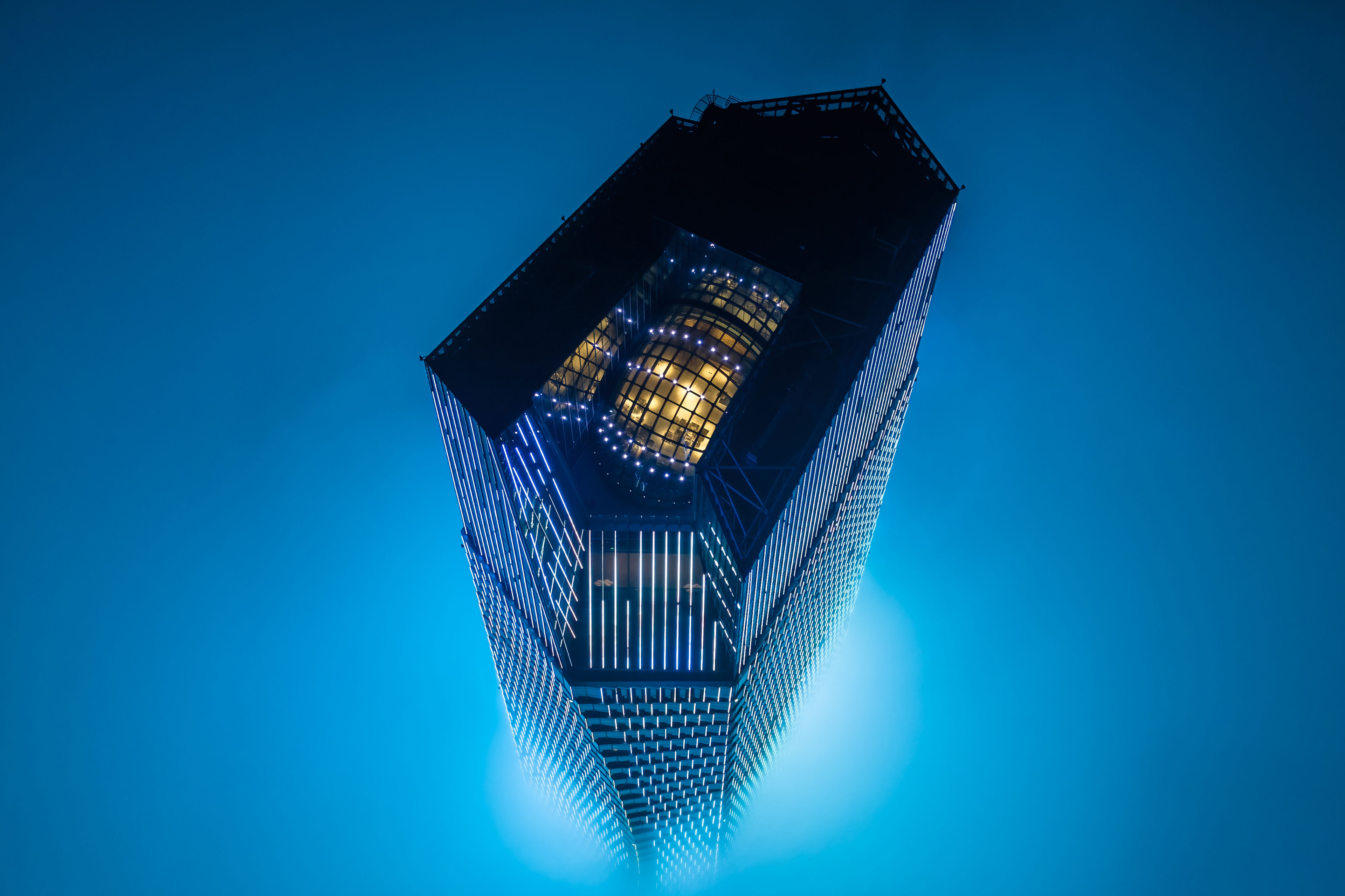 Low‑angle view of a modern illuminated skyscraper against a misty blue sky