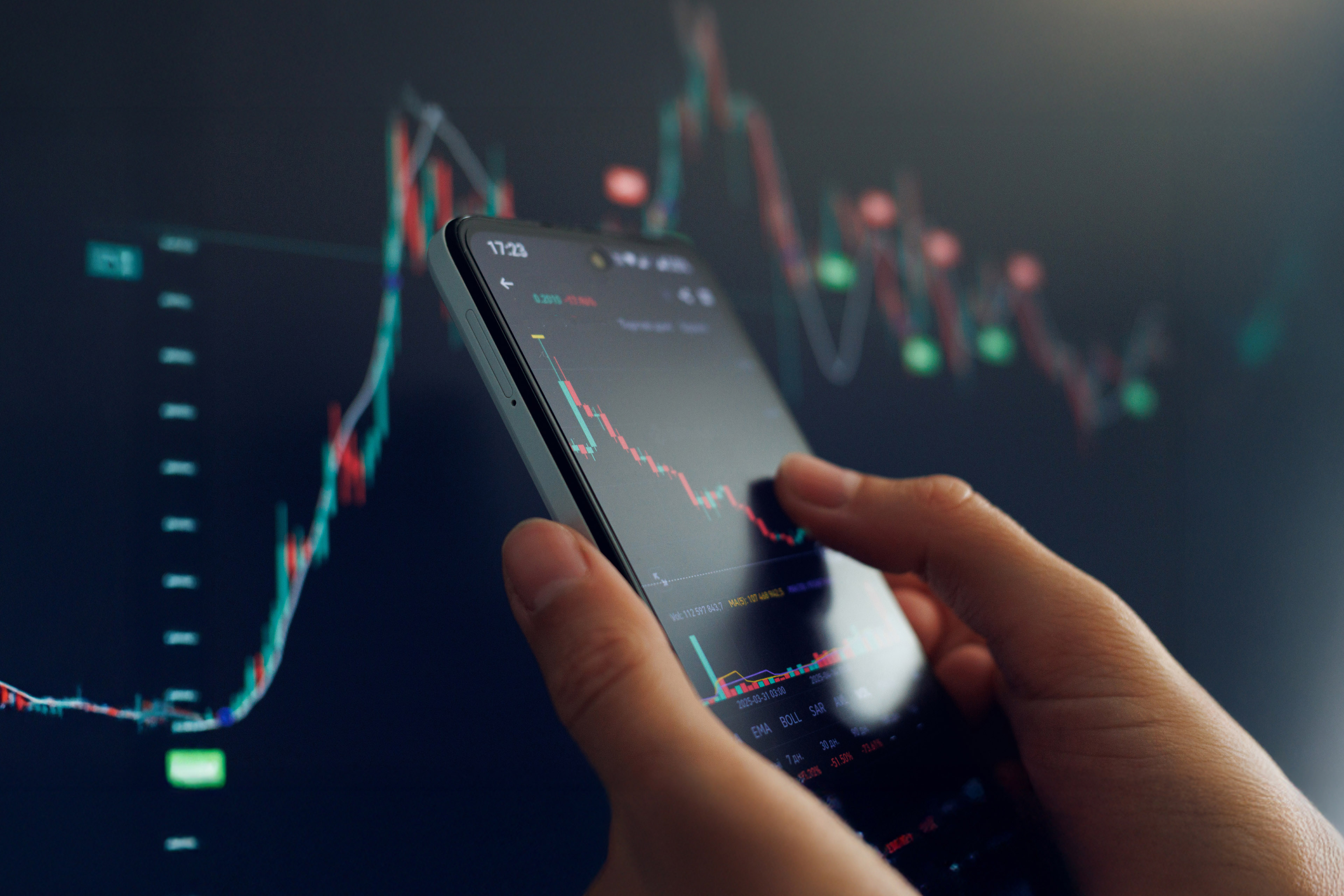 A person examines stock market trends on a smartphone, with colorful charts