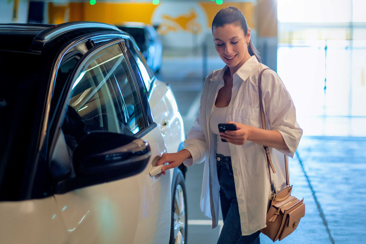 Eine Frau benutzt ihr Handy, während sie eine Autotür öffnet.