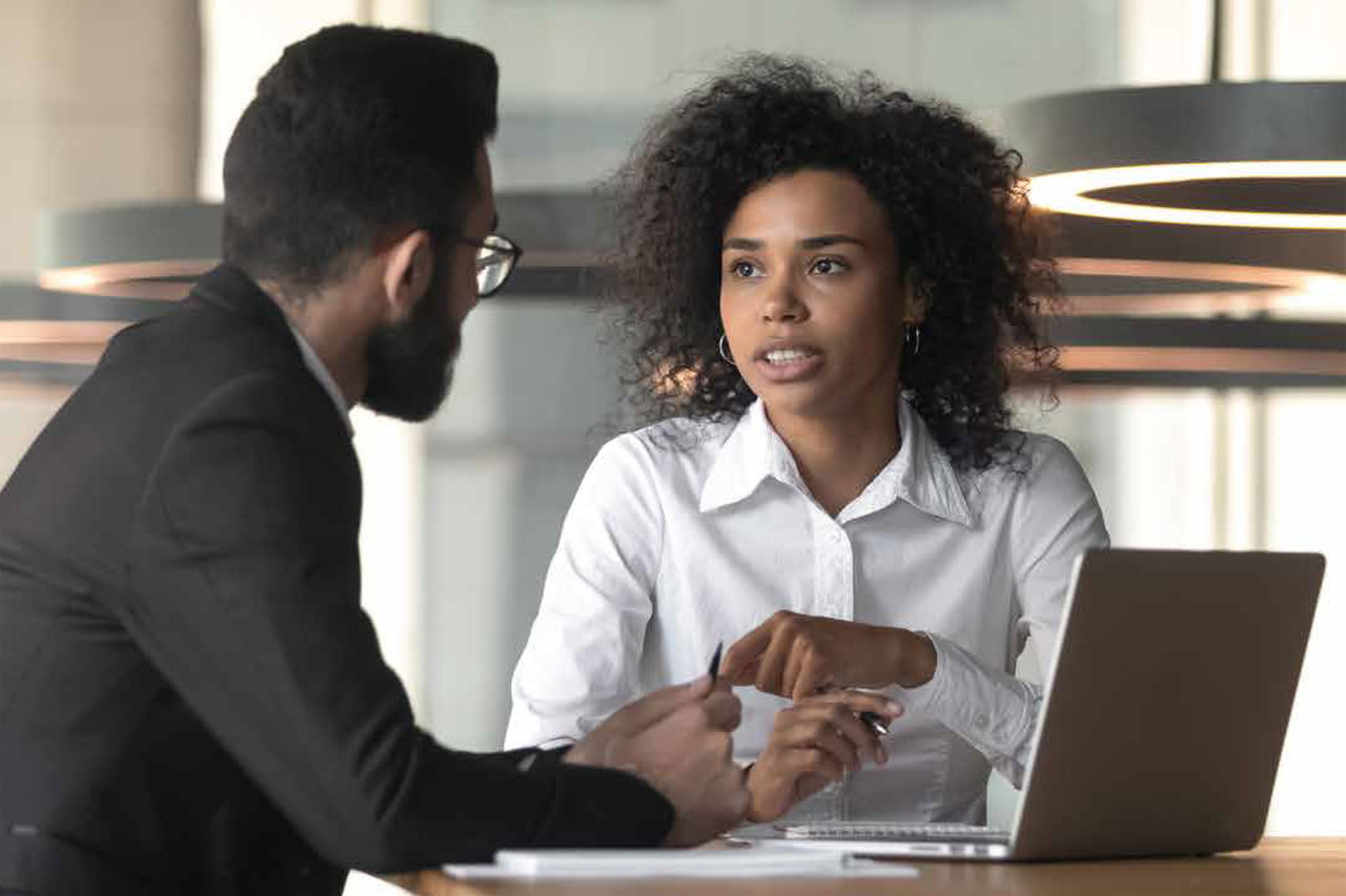 Zwei Personen diskutieren professionelle Themen an einem Tisch mit Laptop.