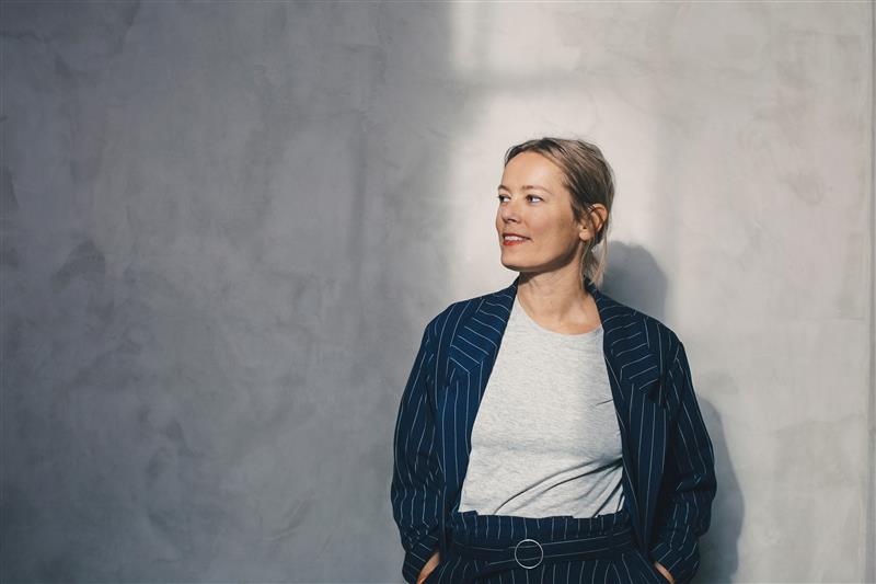 Moderne Businessmode mit Nadelstreifenanzug und lässigem weißen Oberteil vor minimalistischer grauer Wand.